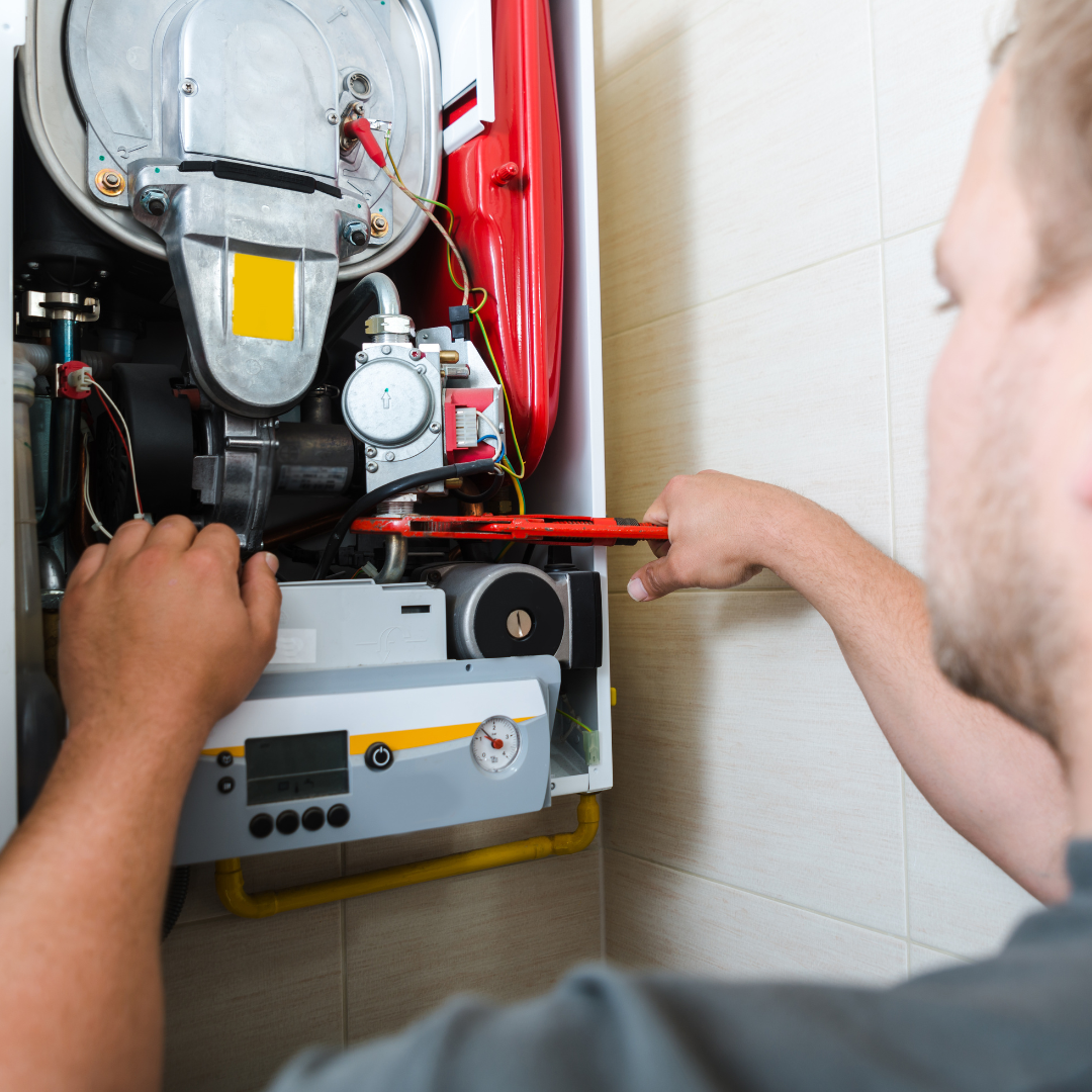A man is fixing a boiler with a wrench.