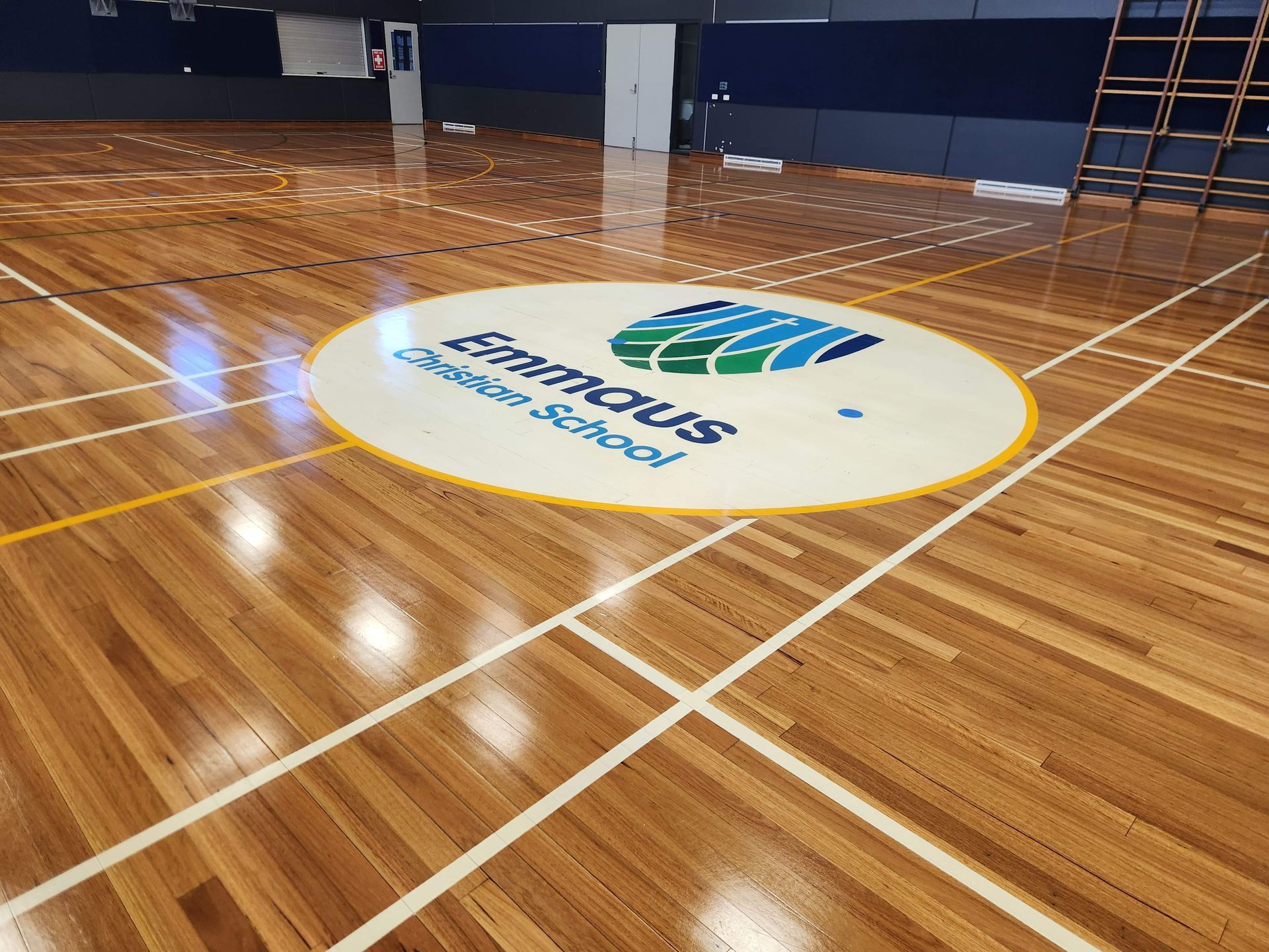 Indoor gym court with polished wood floor and a large circular center logo.
