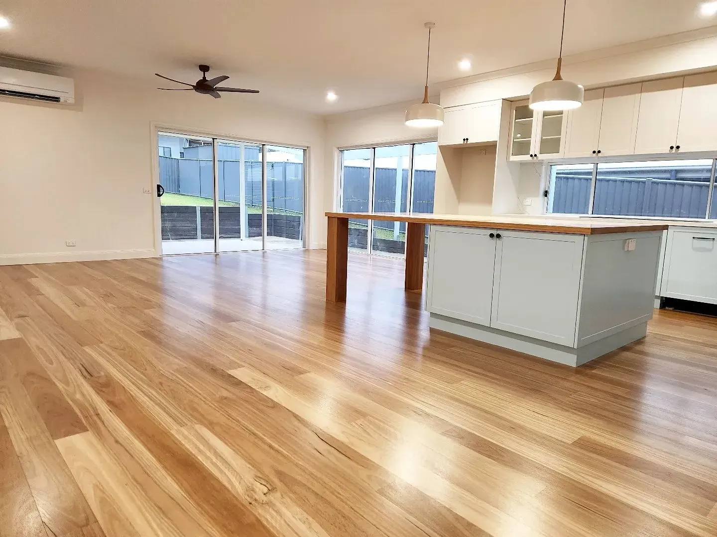 Bright open living room with hardwood floors, kitchen island, and large sliding glass doors overlooking a patio.