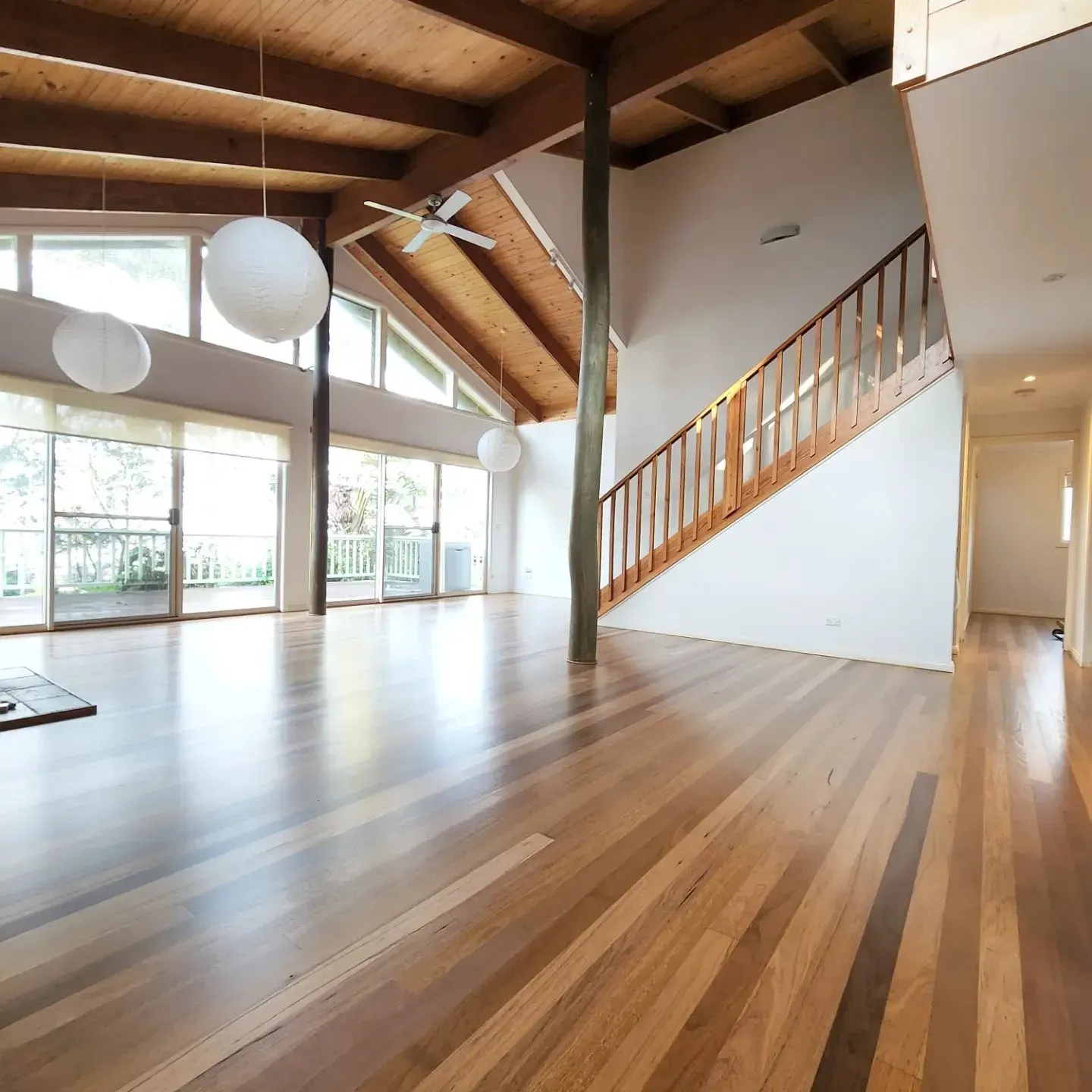 Bright open loft with wood floors, exposed beams, large windows, and a staircase with railing