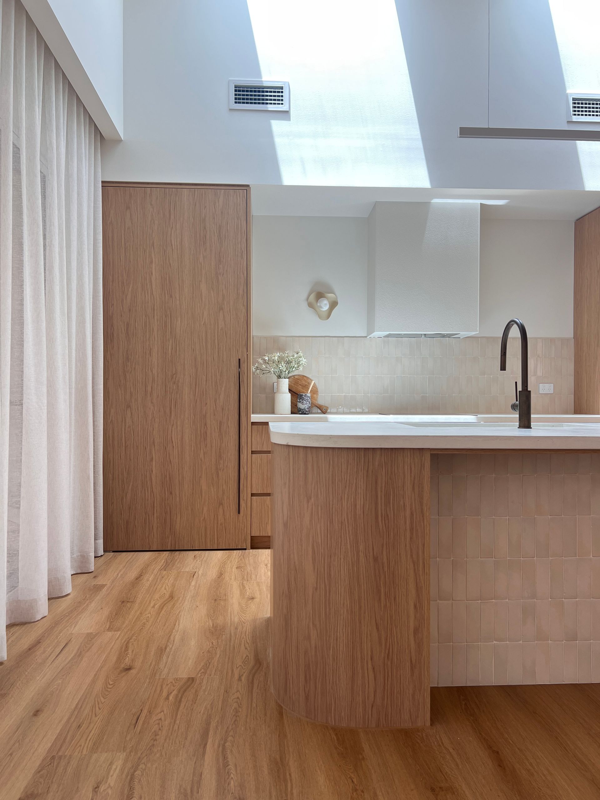 Minimalist kitchen with wood cabinets, white island, and high ceiling with skylight