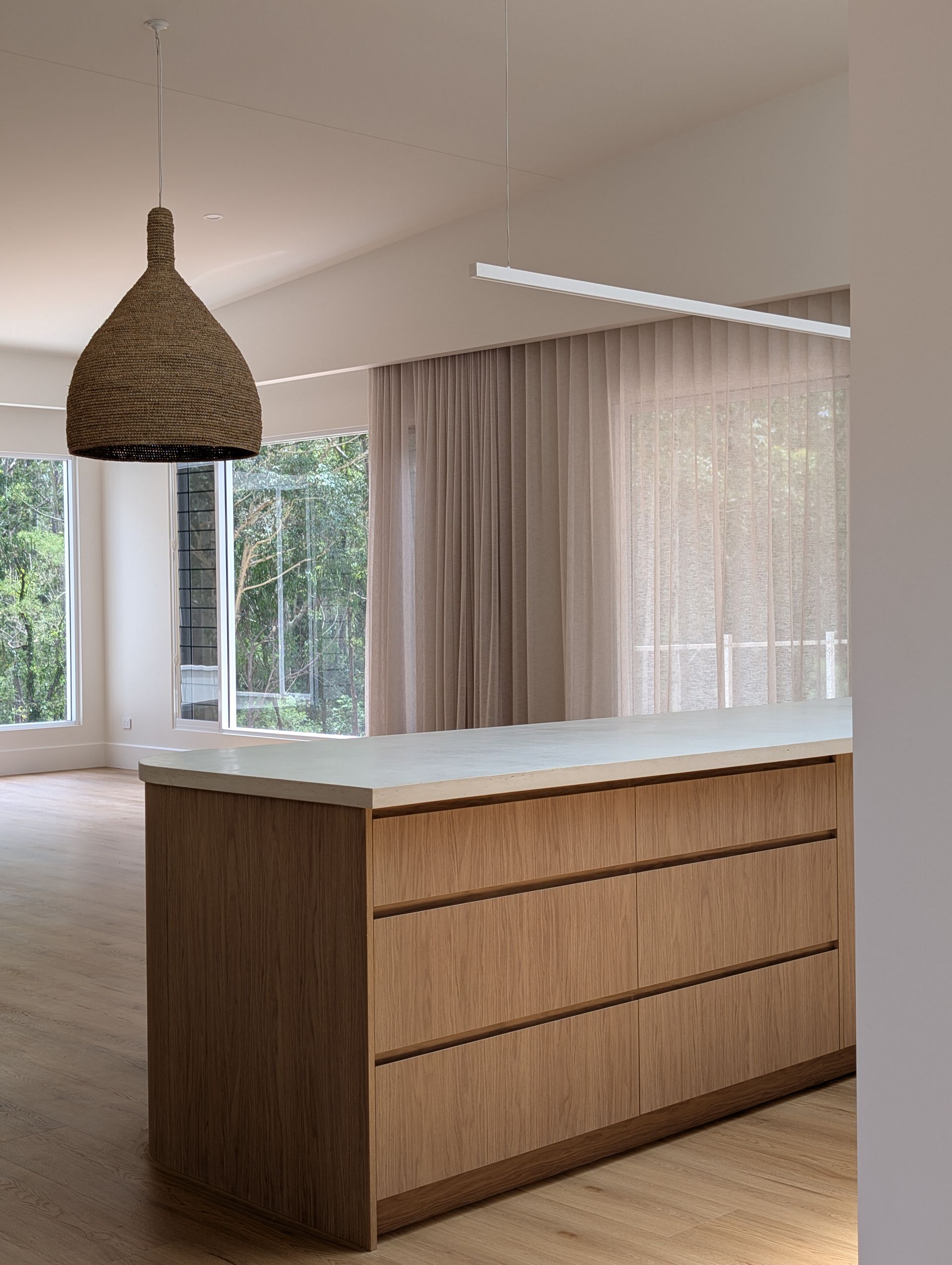 Modern kitchen island with wood paneling, white countertop, and woven pendant light by large windows
