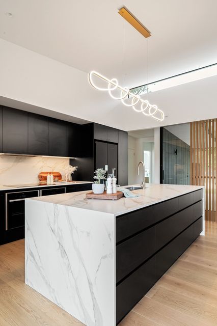 Modern kitchen with marble island, black cabinets, and hanging ring light chandelier
