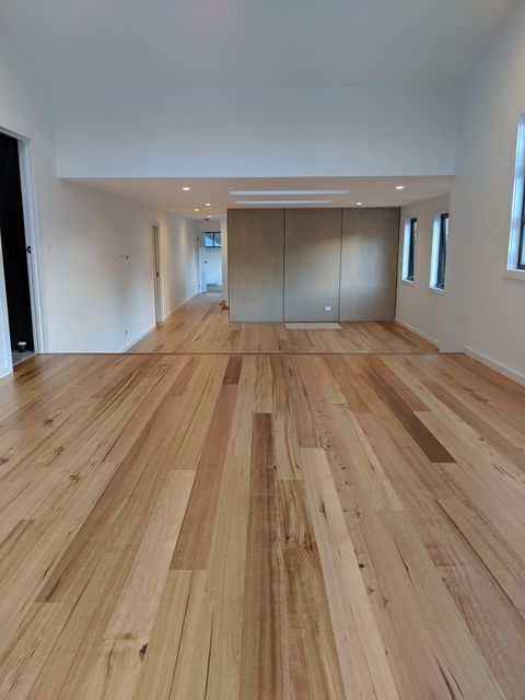 Empty modern room with light wood flooring, white walls, and hallway opening in the distance