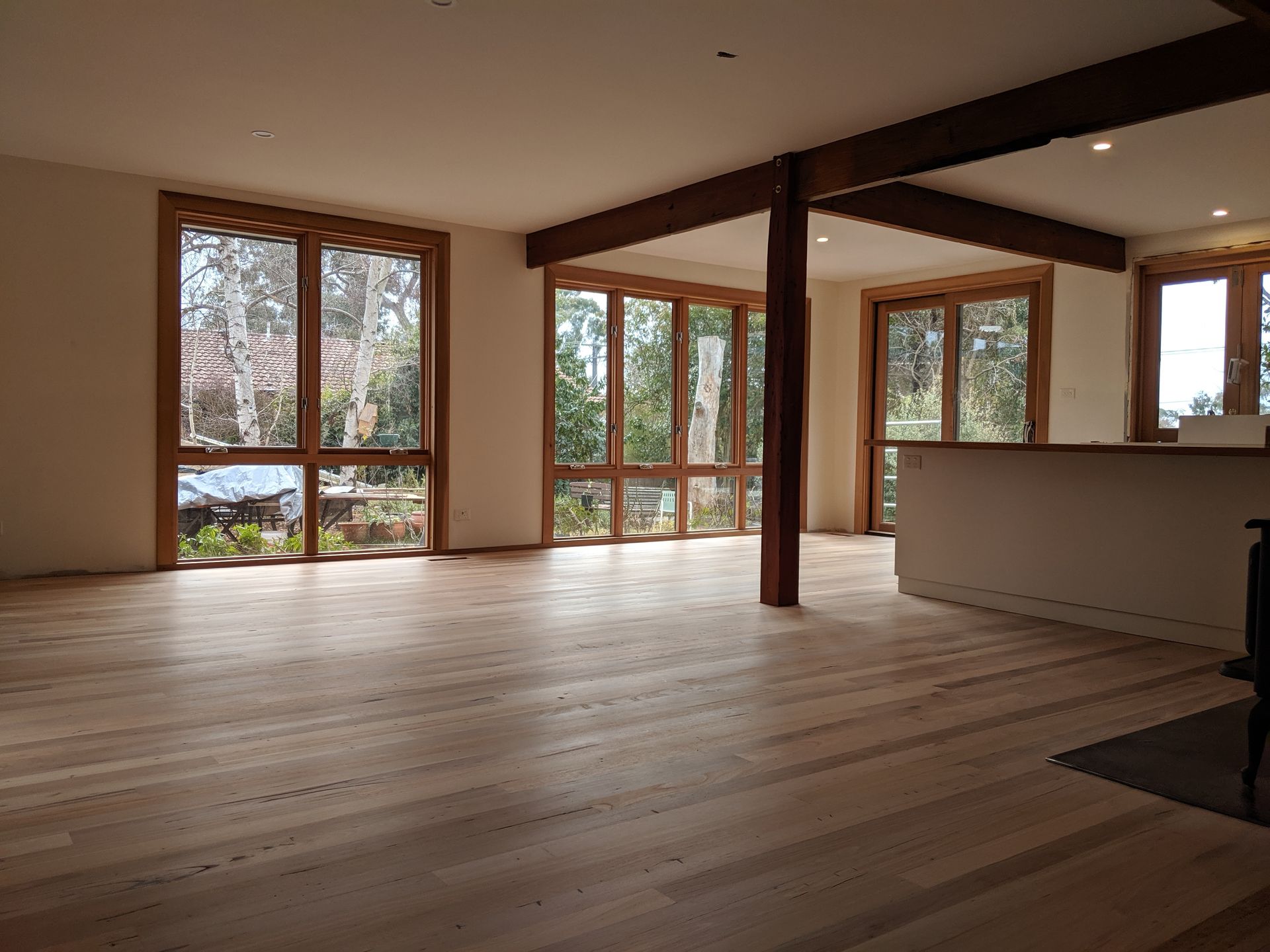 Empty modern living room with large windows, wood floors, and a central support beam