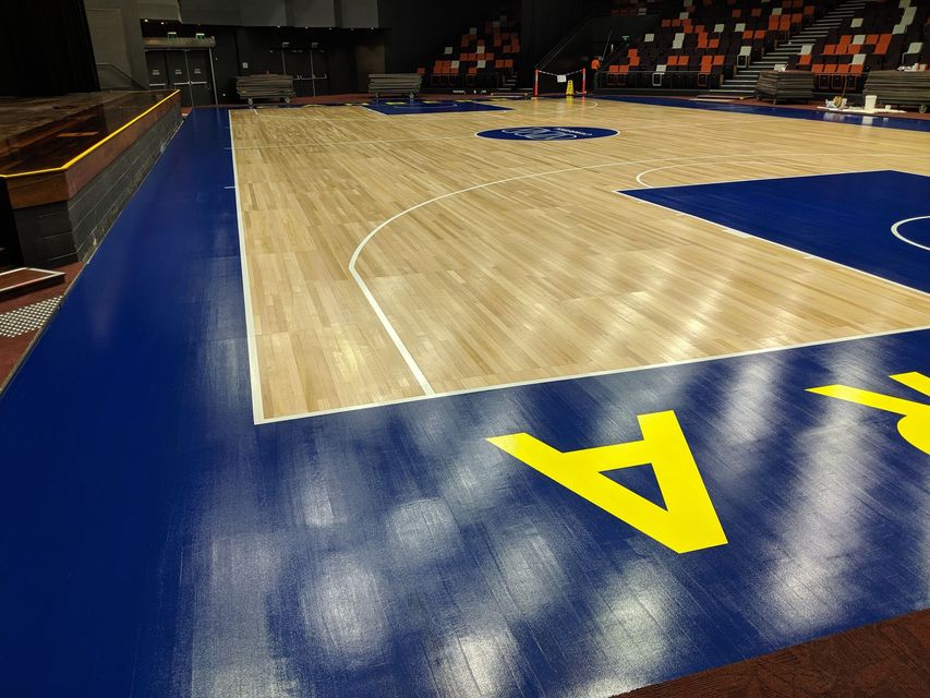 Basketball court sideline with blue and wood flooring, yellow letter A in foreground