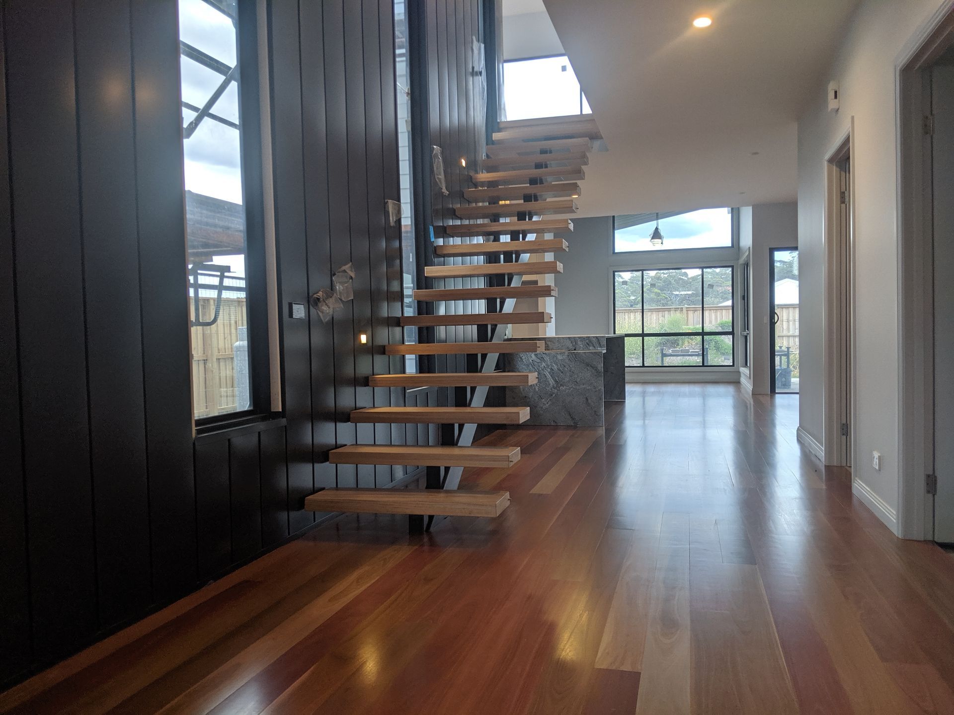 Modern home interior with floating staircase, dark wall paneling, and polished hardwood floors