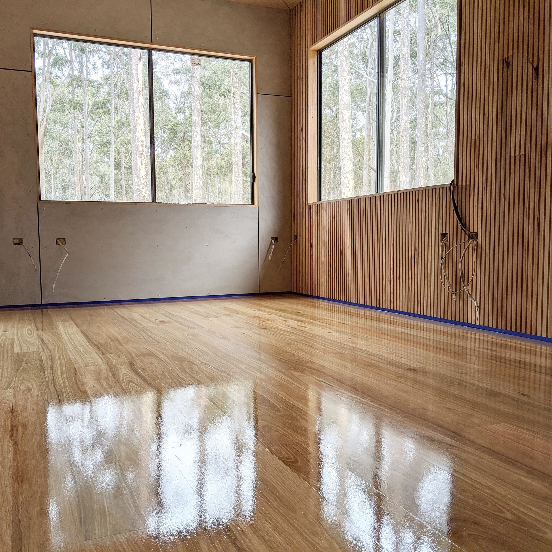 Empty modern room with wood-paneled walls, polished floor, and large windows overlooking trees