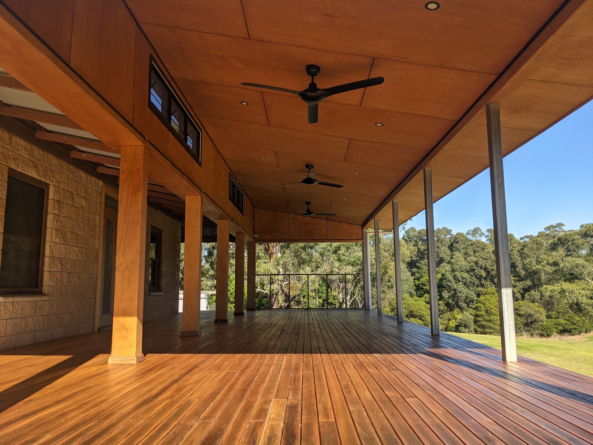 Covered wooden porch with ceiling fans overlooking a green landscape