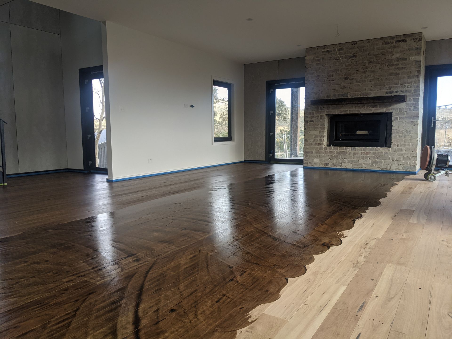 Empty living room with hardwood floors, large windows, and a brick fireplace.