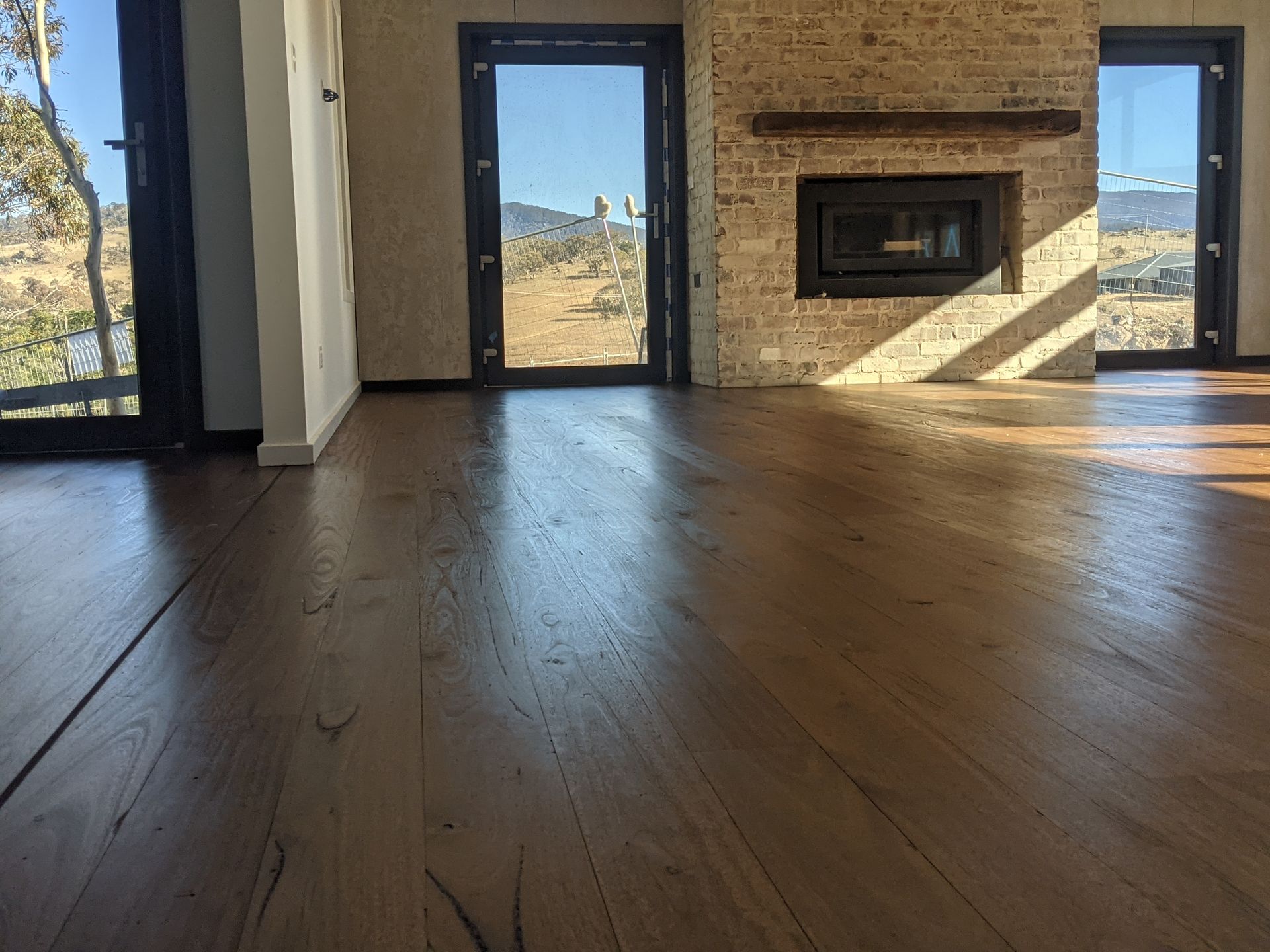Empty living room with wood floors, stone fireplace, and large windows overlooking a desert view