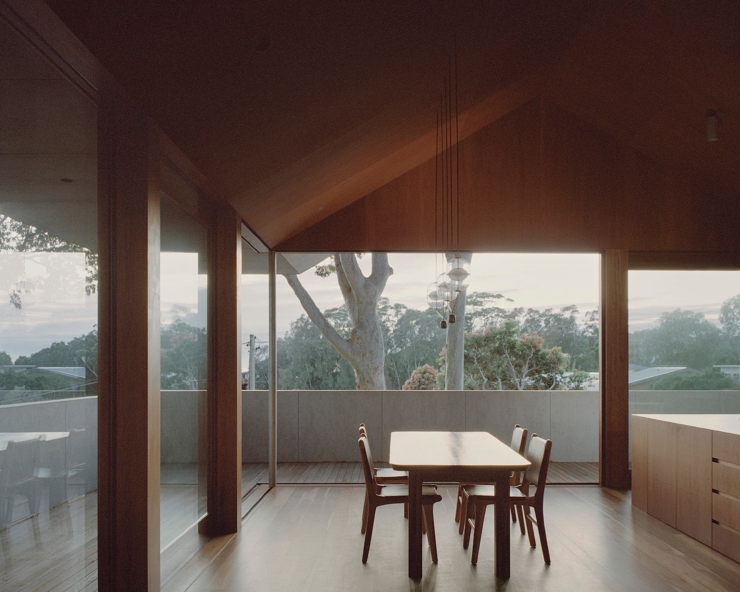 Modern dining room with wooden table, chairs, large windows, and a view of trees and water