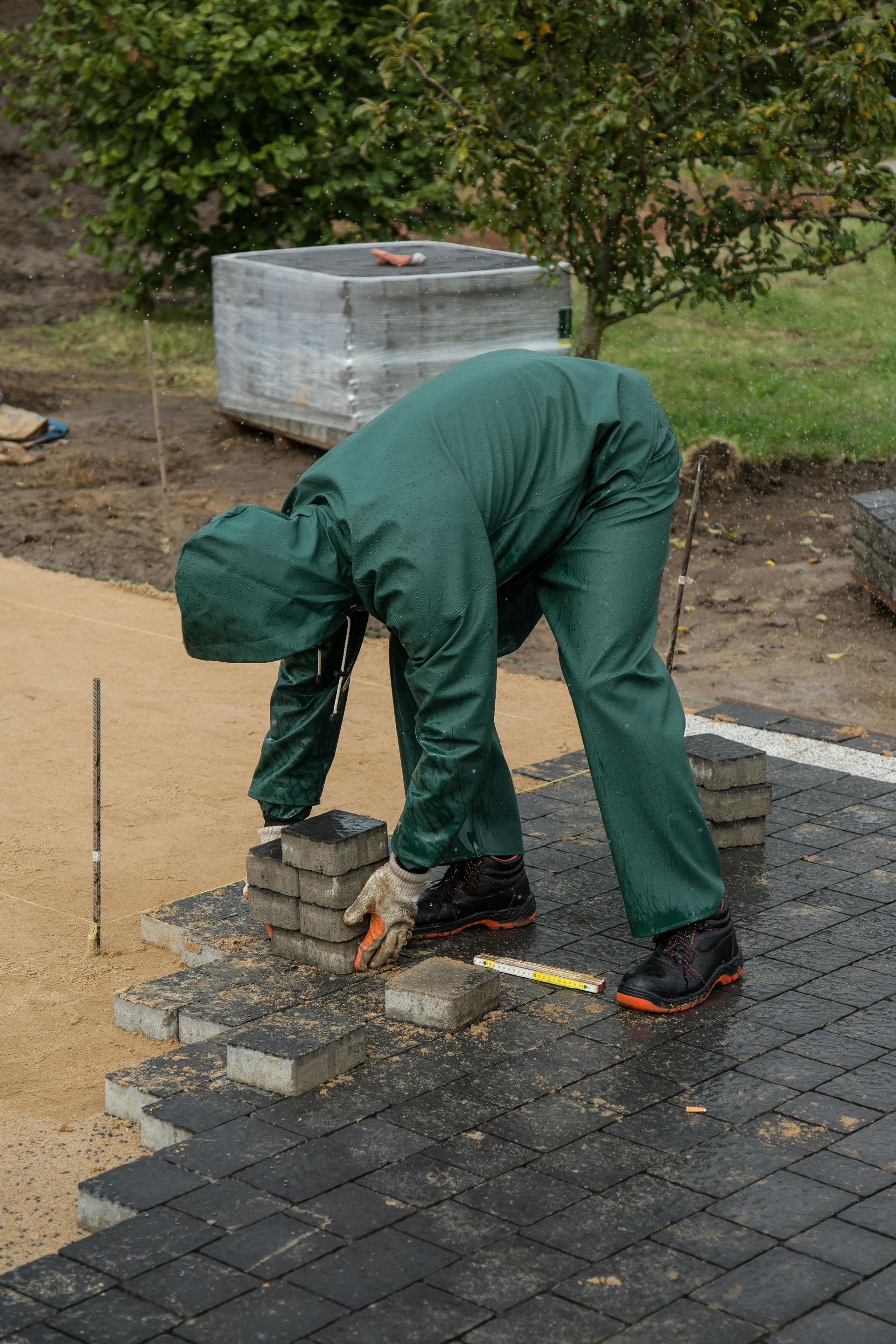 A man in a green suit is laying bricks on the ground.