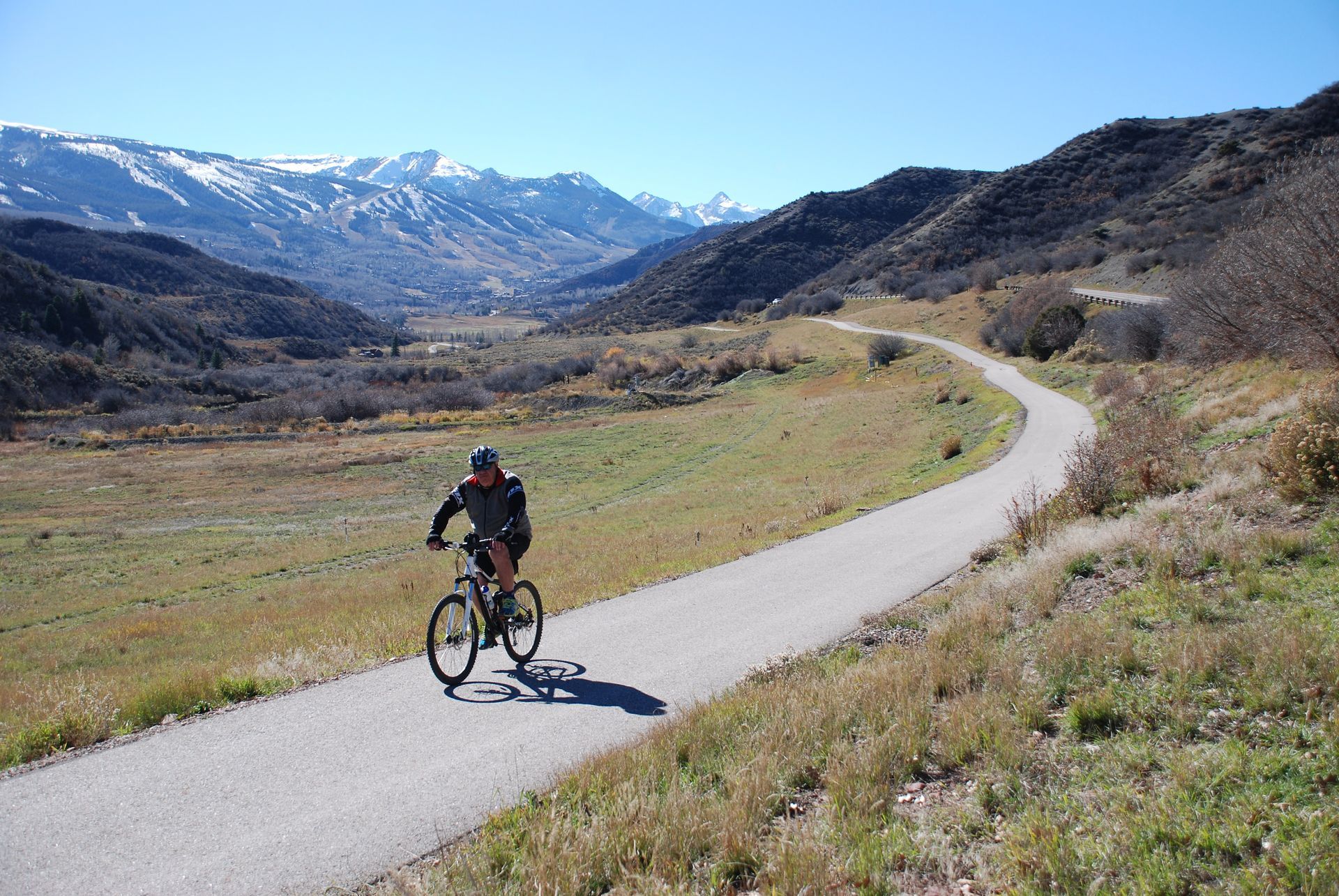 Cyclist riding on a winding mountain road with snowy peaks and grassy valley in the background in brush creek  with slow & say hello in colorado
