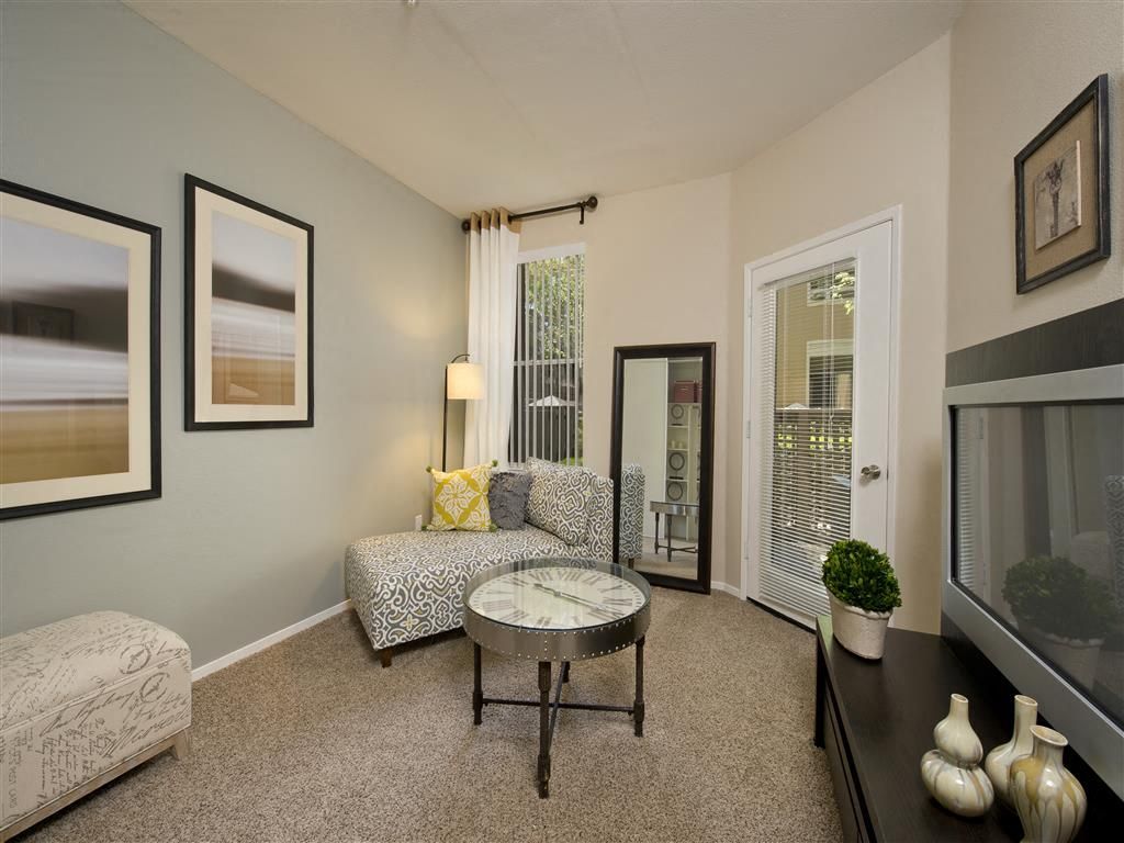 Living room with a gray patterned chair, round glass coffee table, mirror, and French doors at Rosewalk Apartment Homes in San Jose, CA.