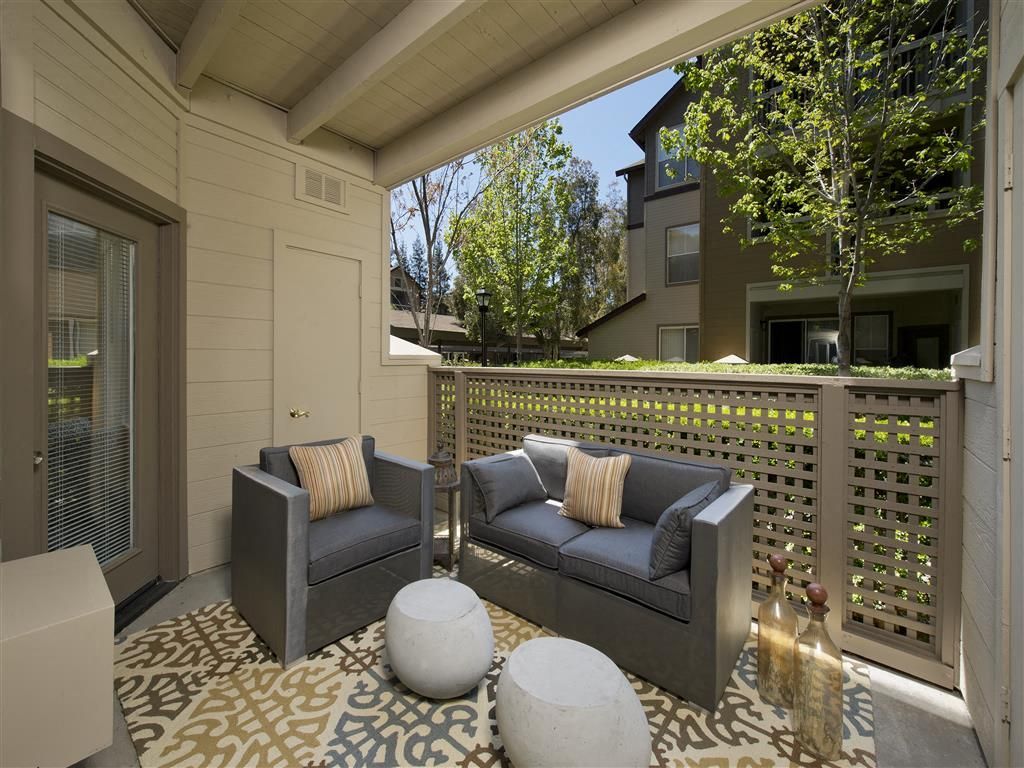 Outdoor apartment balcony with gray seating, cushions, and lattice railing at Rosewalk Apartment Homes in San Jose, CA.