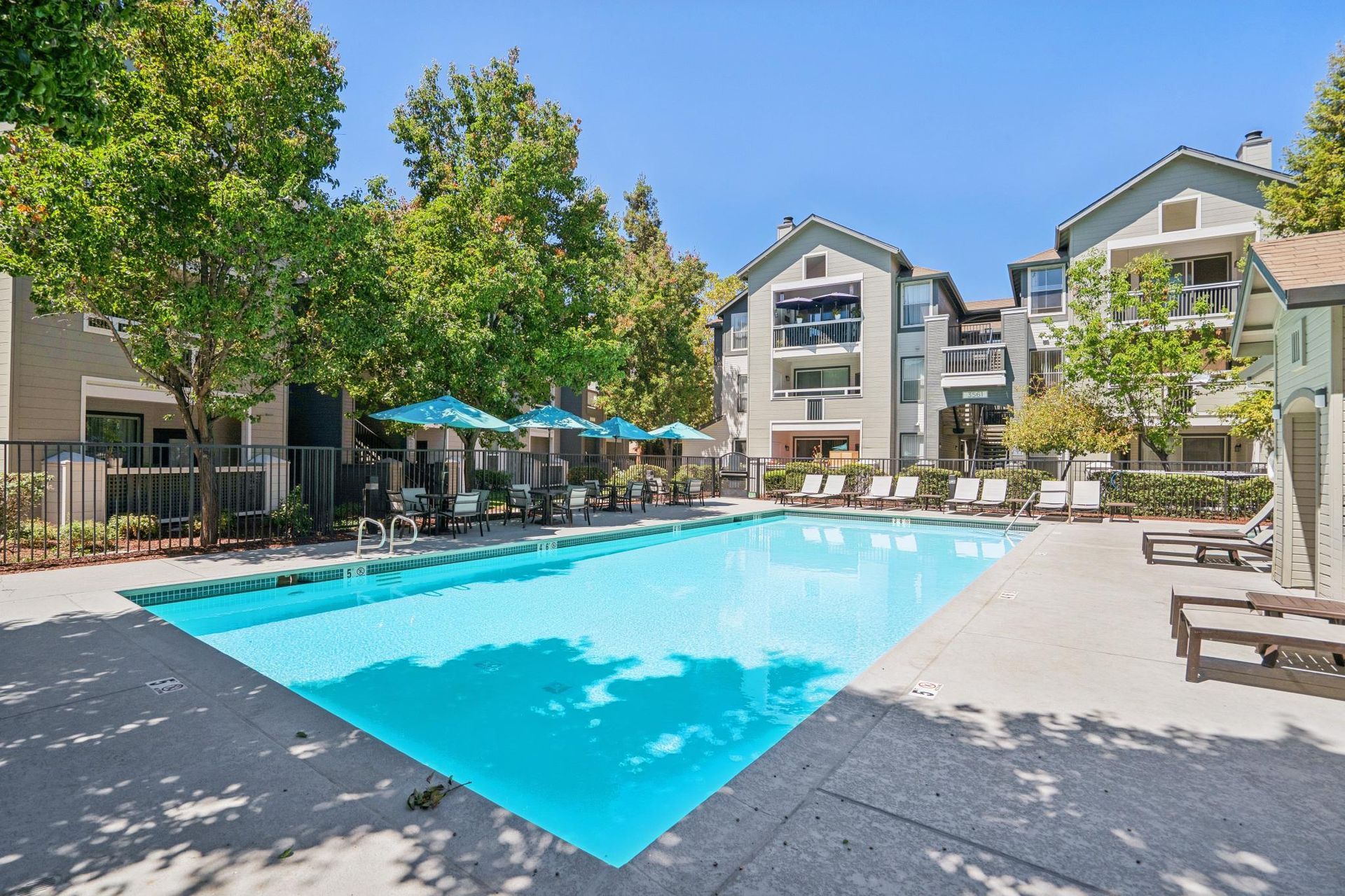 Apartment complex pool with turquoise water, lounge chairs, and patio umbrellas in a sunny courtyard