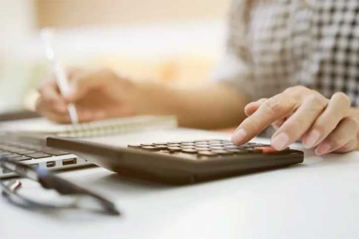 Hands using a calculator and writing on paper at a desk