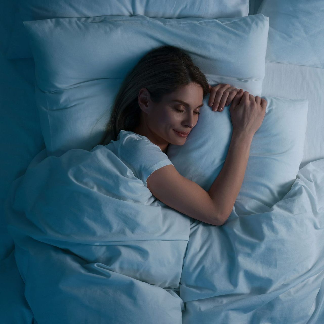 A woman is sleeping in a bed with white sheets and pillows A woman is sleeping in a bed with white sheets and pillows