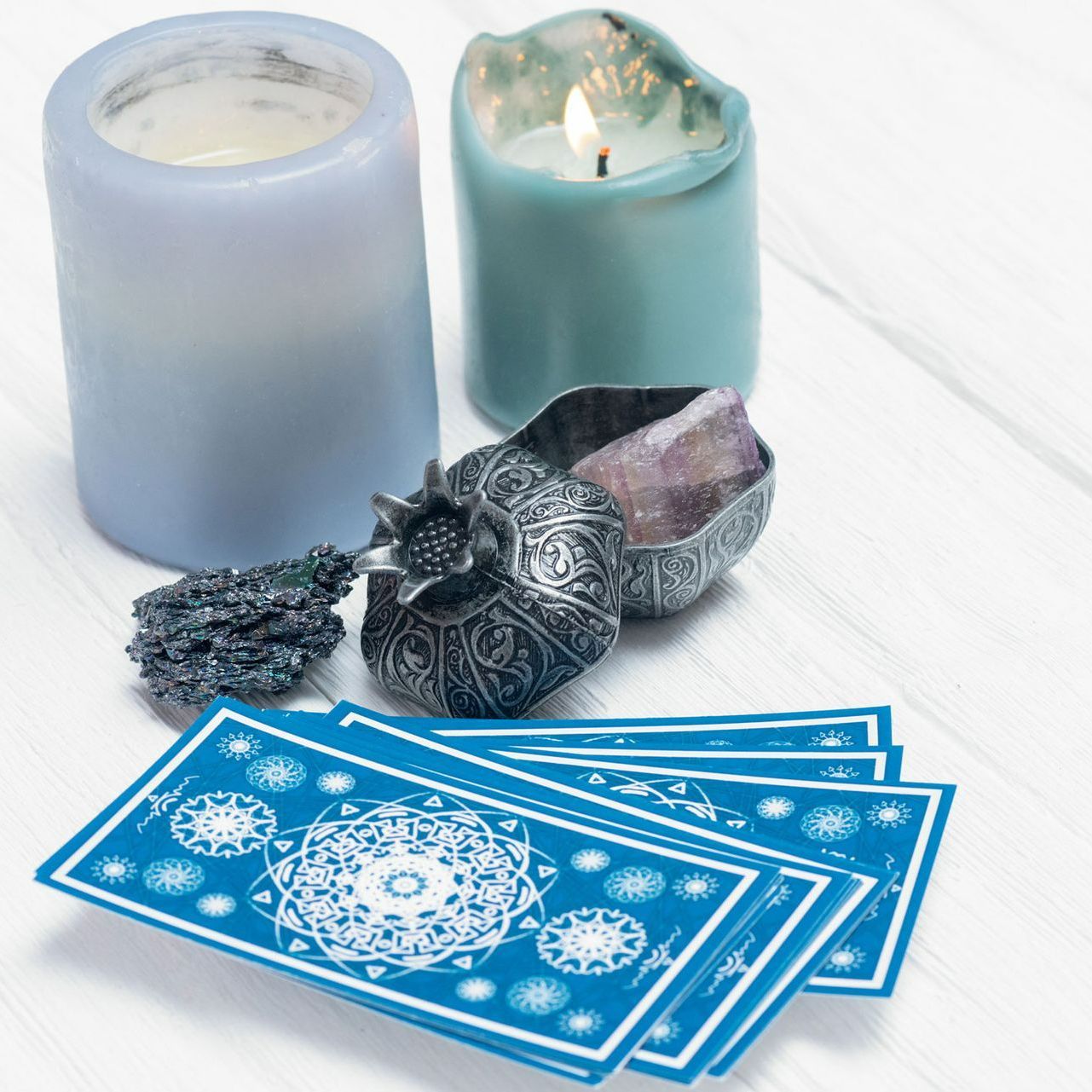 A stack of blue tarot cards sits on a table next to candles and crystals