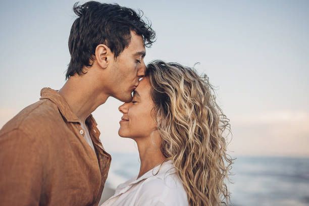 A man is kissing a woman on the forehead on the beach.