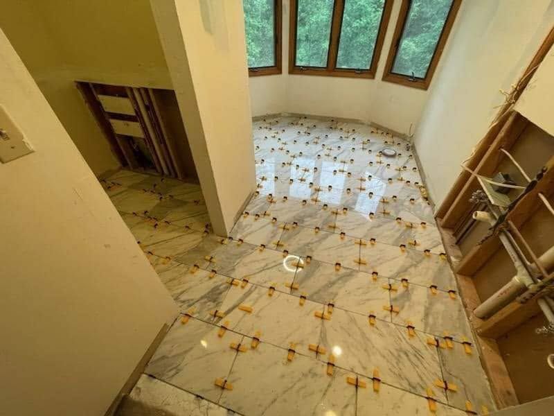 Empty tiled room with large windows and a doorway, viewed from above.