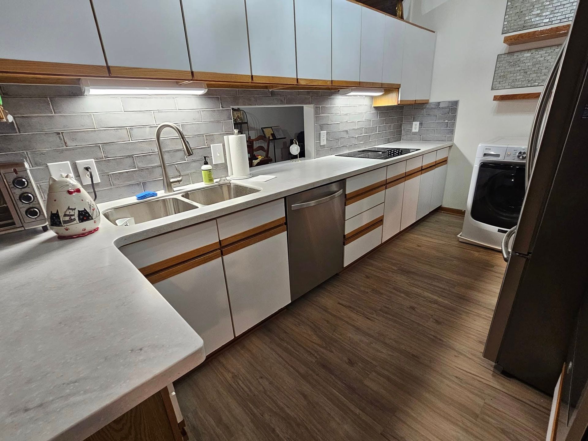Modern kitchen with white cabinets, gray backsplash, stainless appliances, and wood-look flooring.