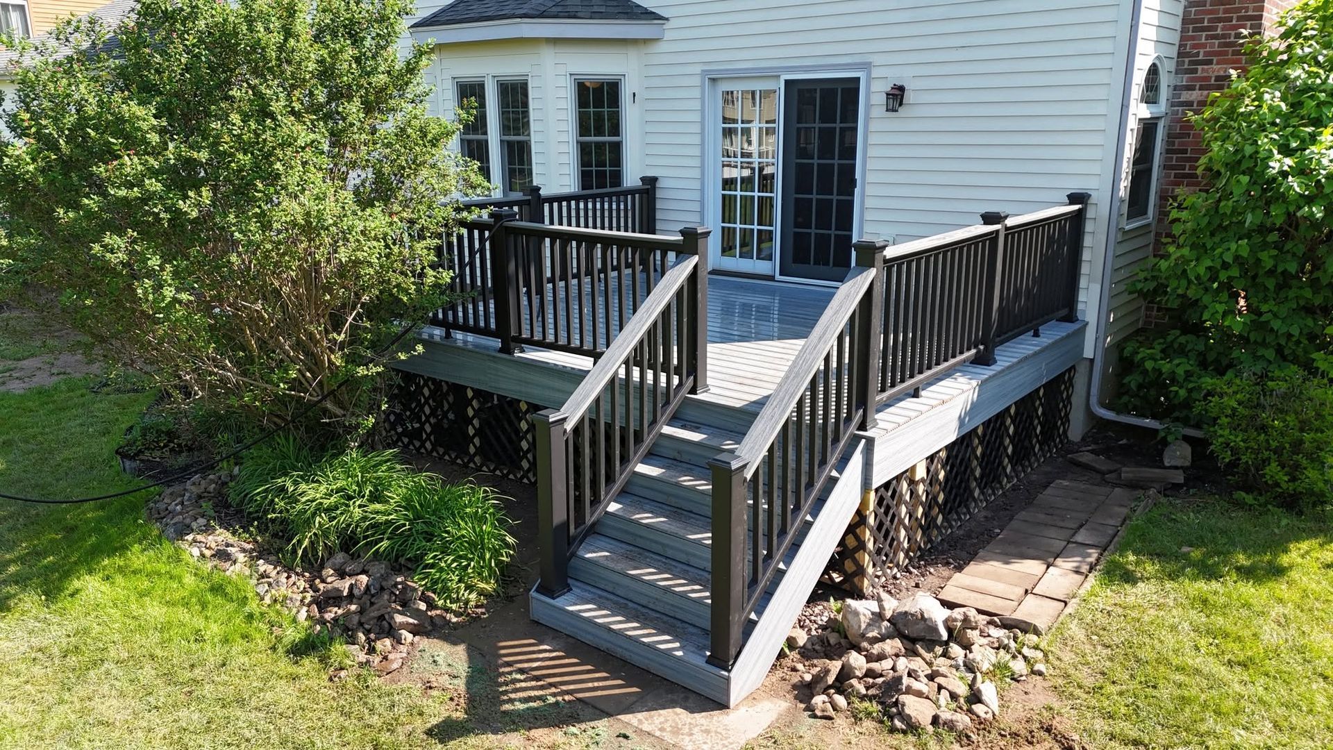 White house back deck with gray stairs, black railings, and surrounding green shrubs