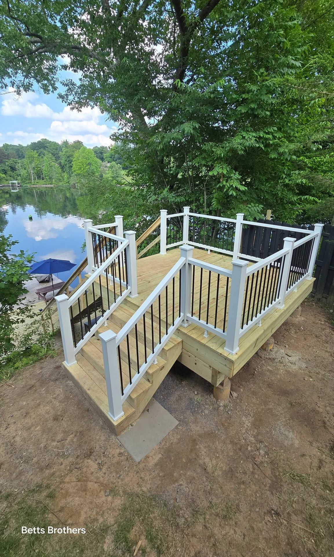 Wooden lake overlook deck with white railings and stairs among trees beside calm water
