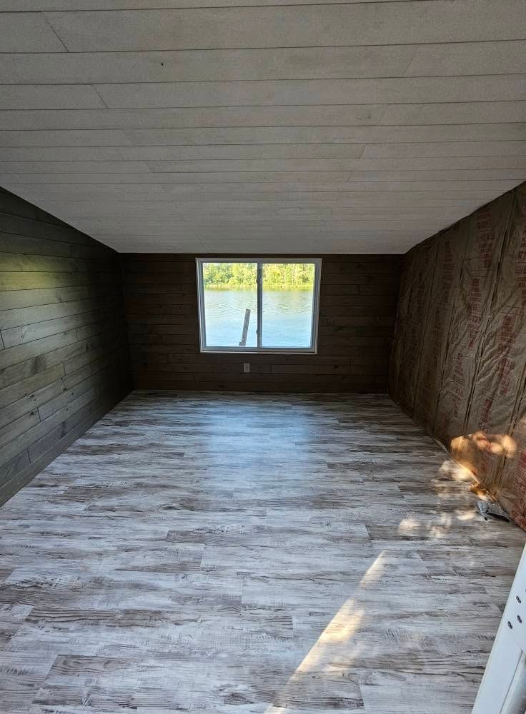 Empty room with wood-paneled walls, gray floor, and a small window at the far end.