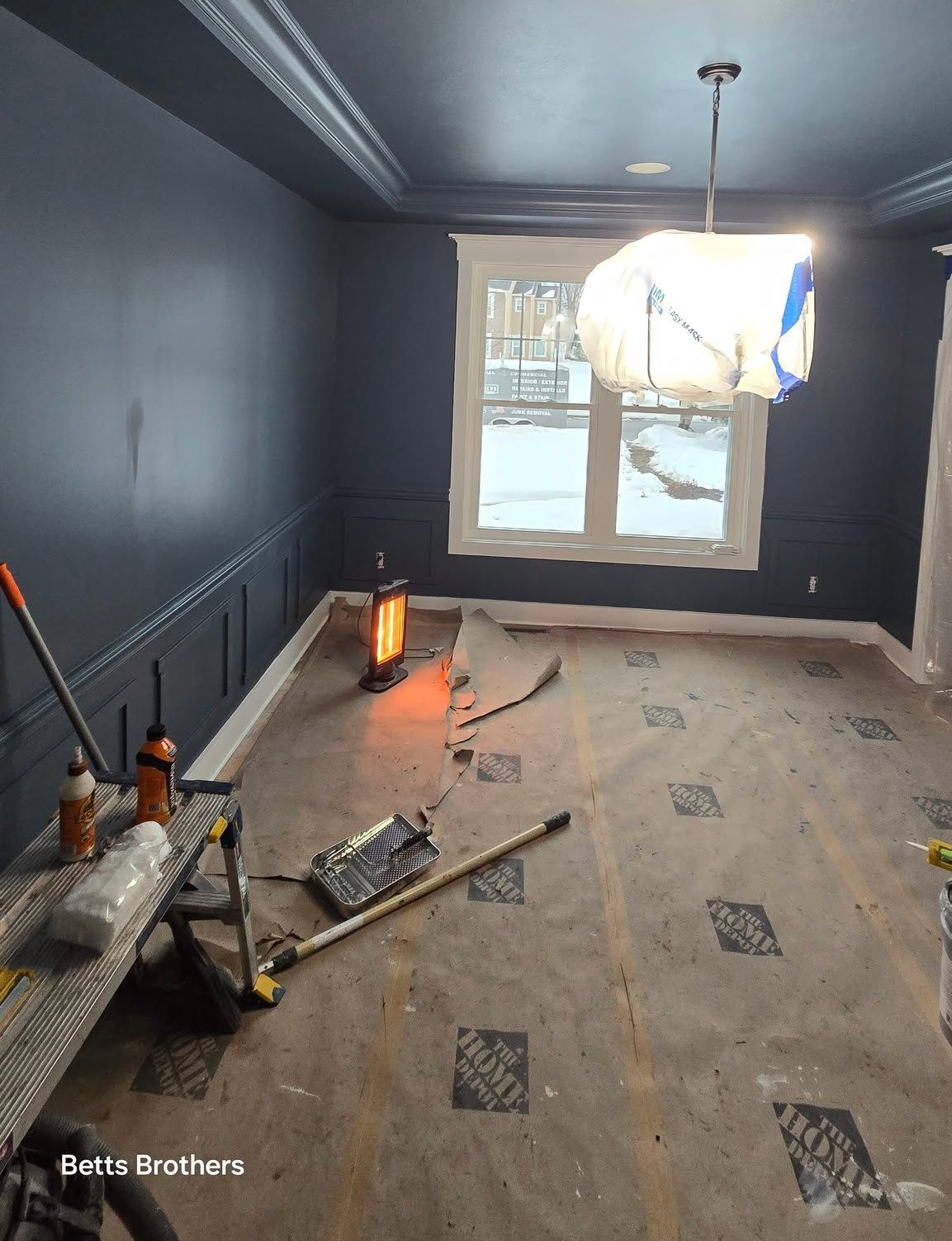 Small room under renovation with dark walls, scattered tools, and daylight through a window.