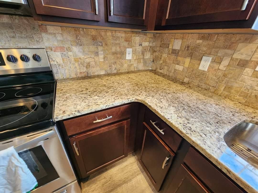 Corner kitchen with tan granite countertops, dark wood cabinets, and stainless steel appliances.