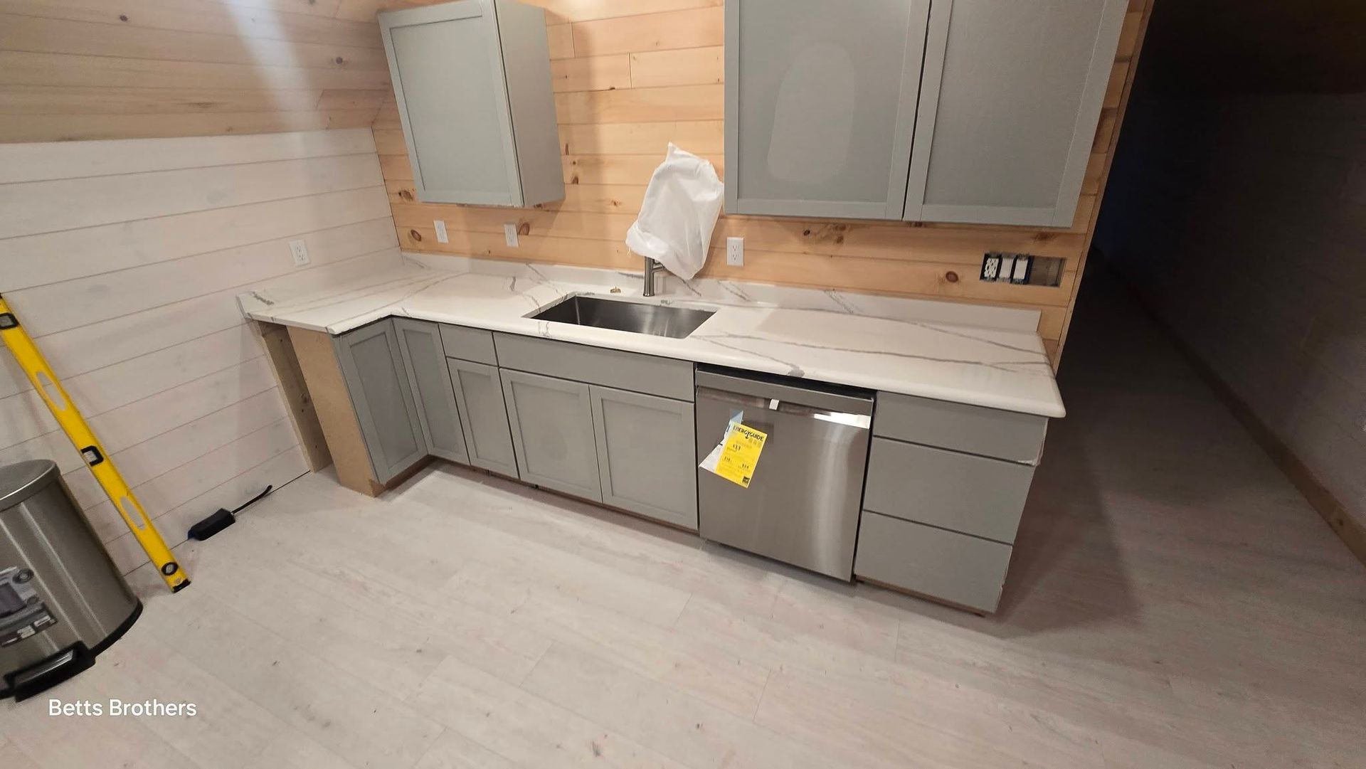 Modern kitchen with gray cabinets, white countertops, and wood-paneled walls under construction