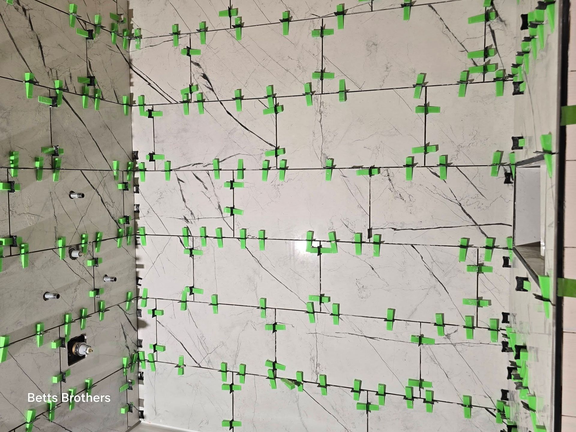 Concrete wall with many green climbing holds and dangling ropes, viewed from below.