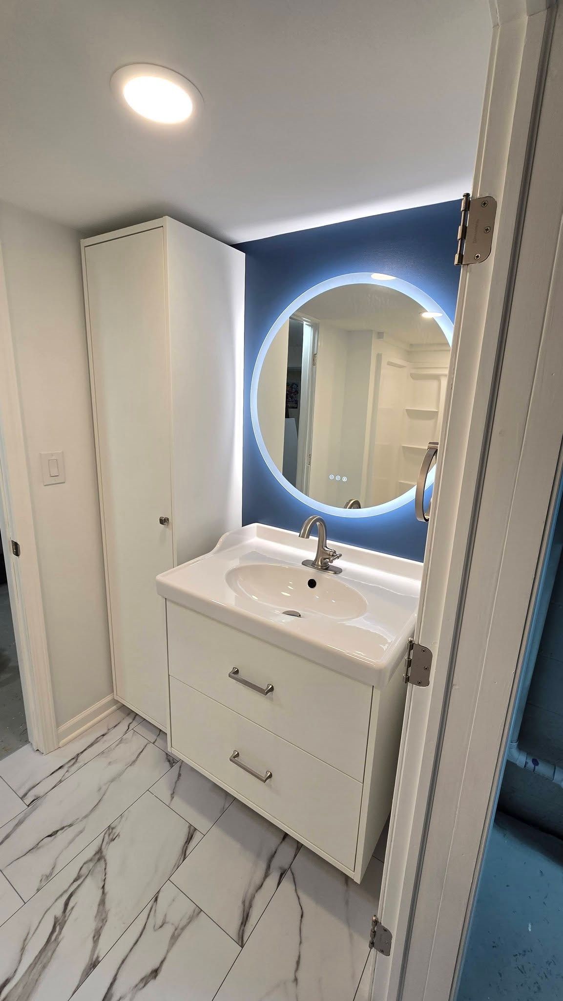 Modern white bathroom vanity with round lit mirror and marble-pattern floor tiles