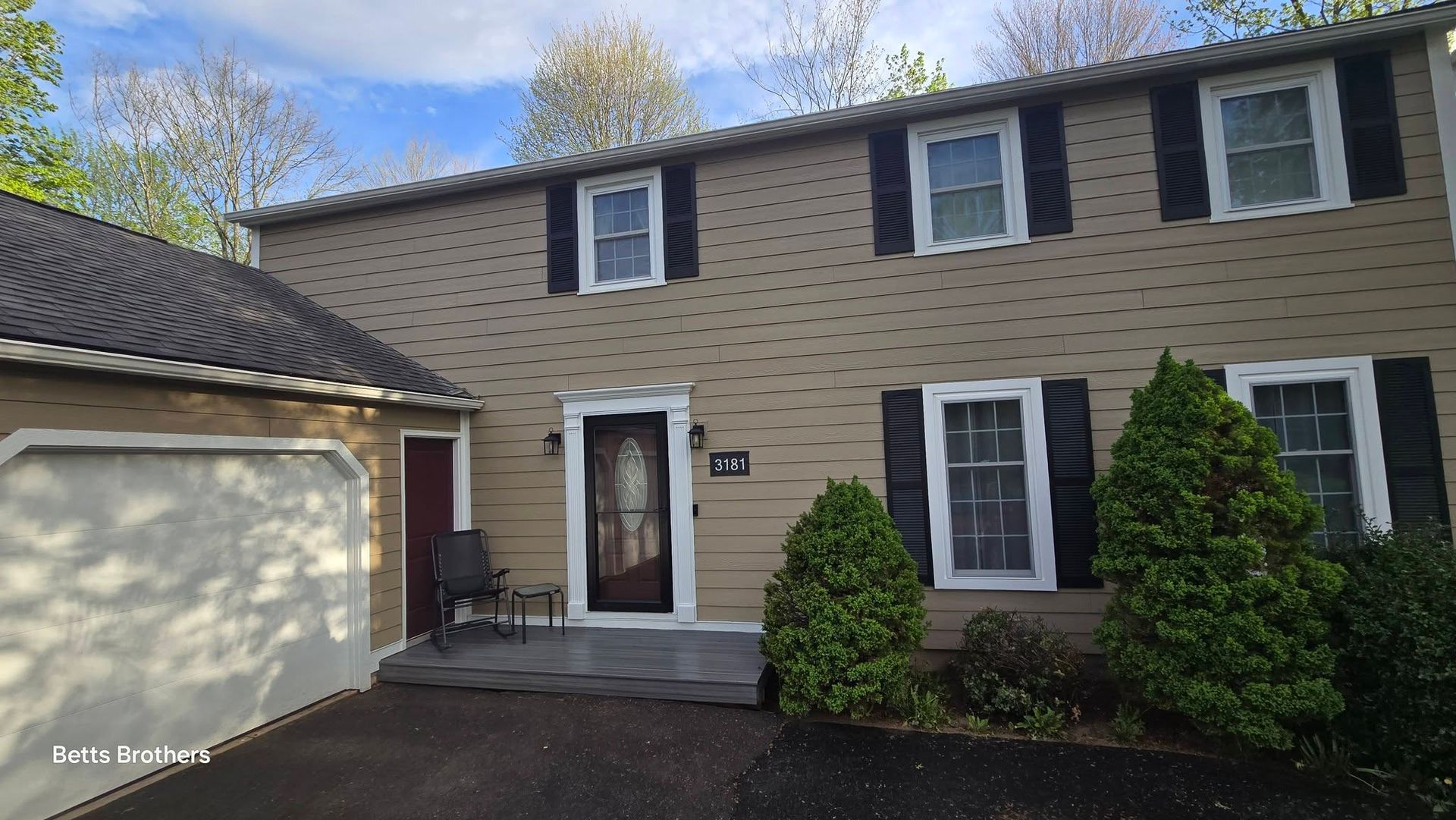 Two-story beige house with dark shutters, front door, garage, and driveway on a sunny day