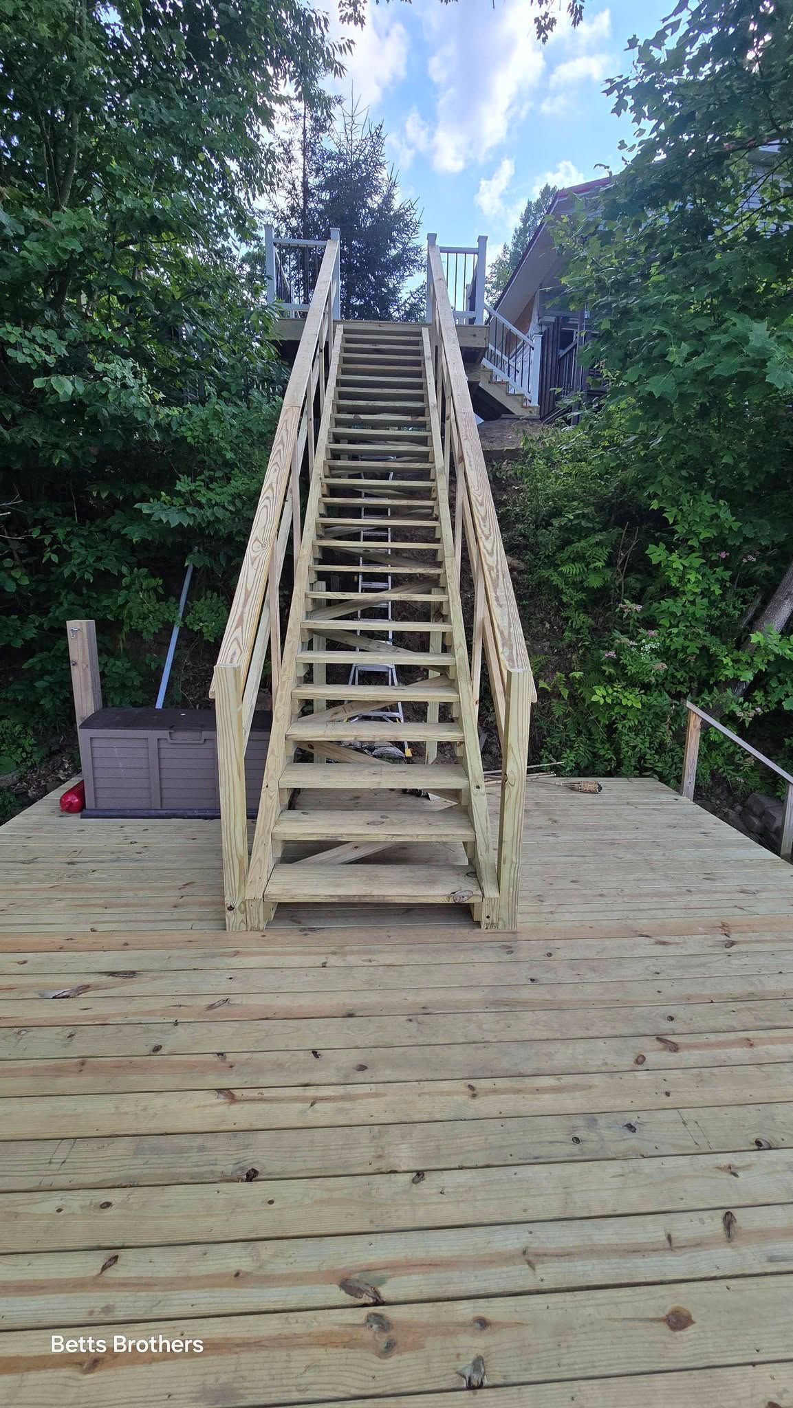 Wooden staircase rising from a deck into dense green trees, with a hot tub on the left.
