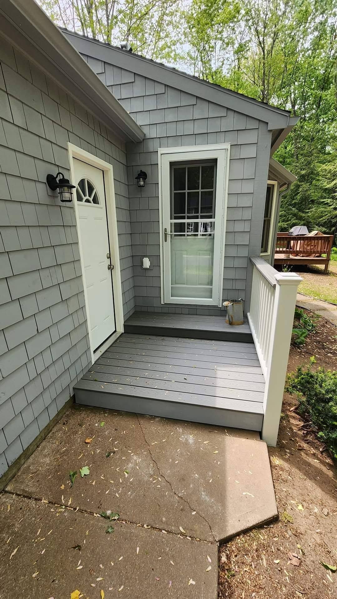 Gray house entrance with small porch, white railings, and a ramp leading to a glass door