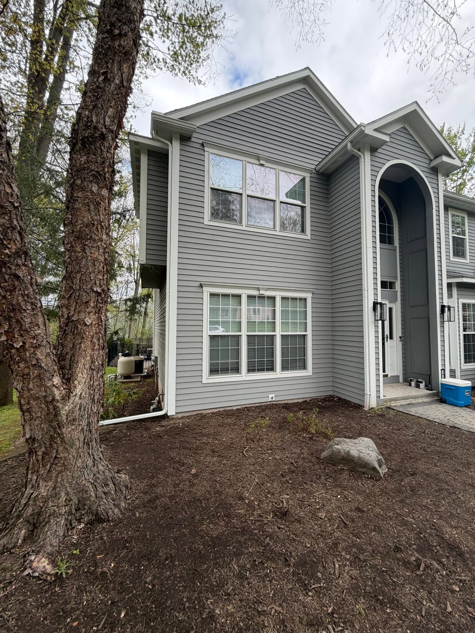 Gray two-story townhouse exterior with white trim, windows, and a covered entry beside a tree.