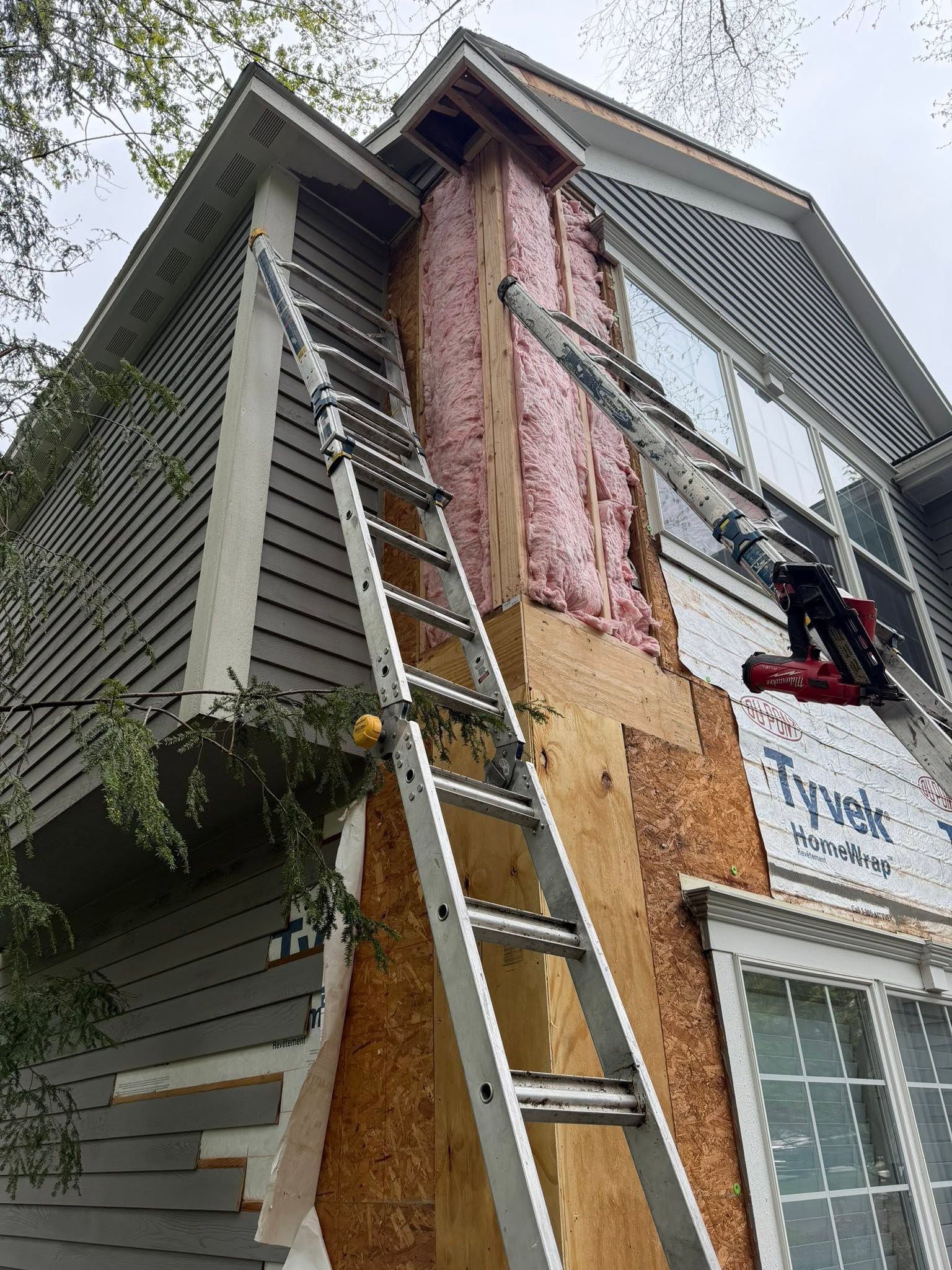 Ladder leaning against a house with exposed pink insulation and new siding being installed