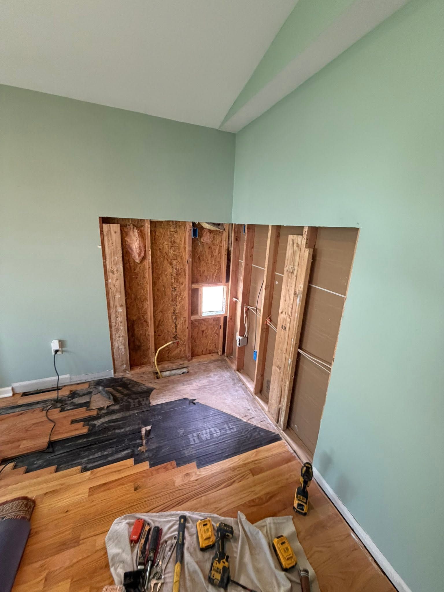 Partially gutted room with exposed studs, torn flooring, and mint-green walls during renovation
