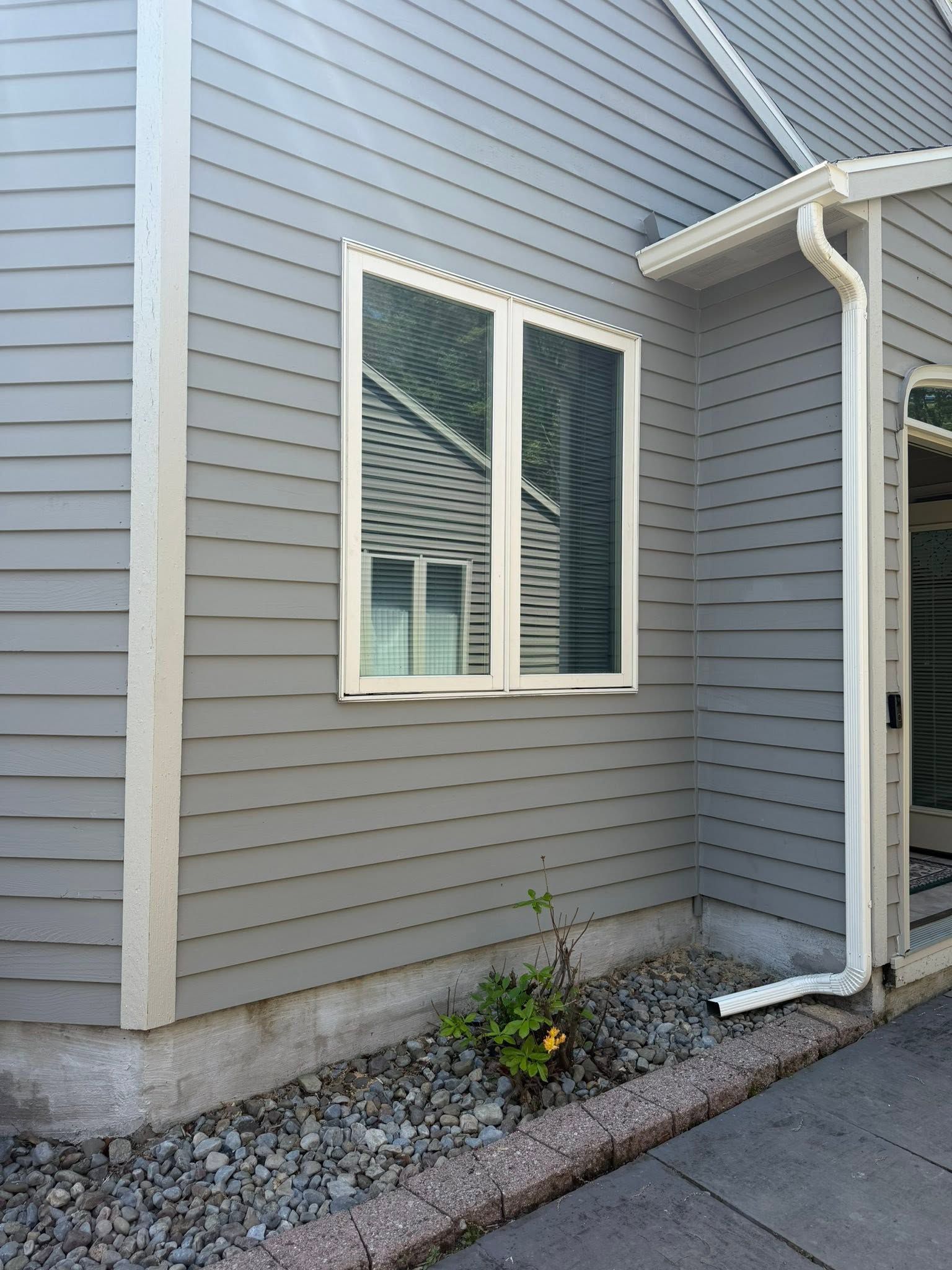 Gray house exterior with a white-trimmed window, gravel bed, and small plant