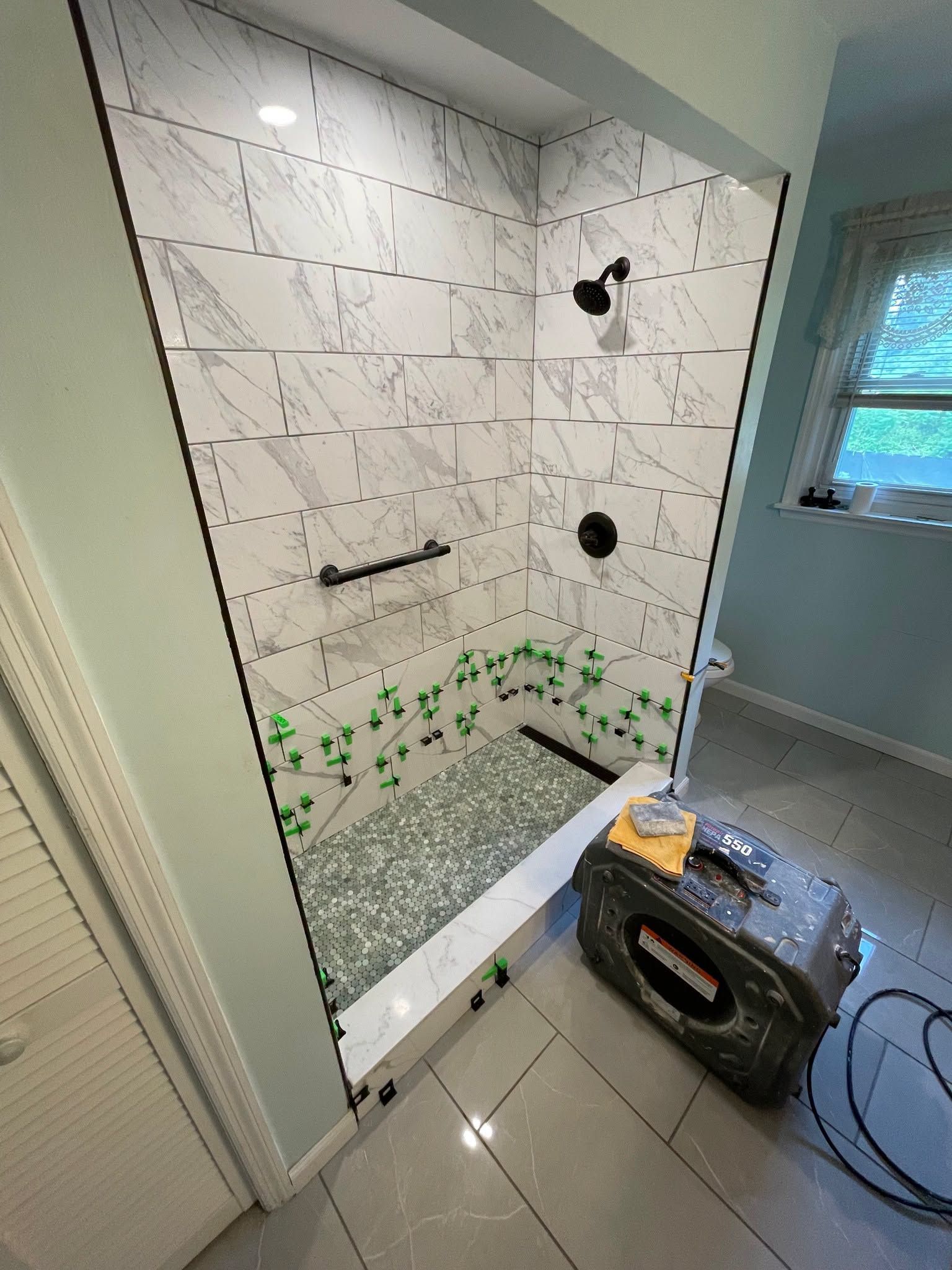Partially tiled shower under construction with a bucket, tools, and a window on the right