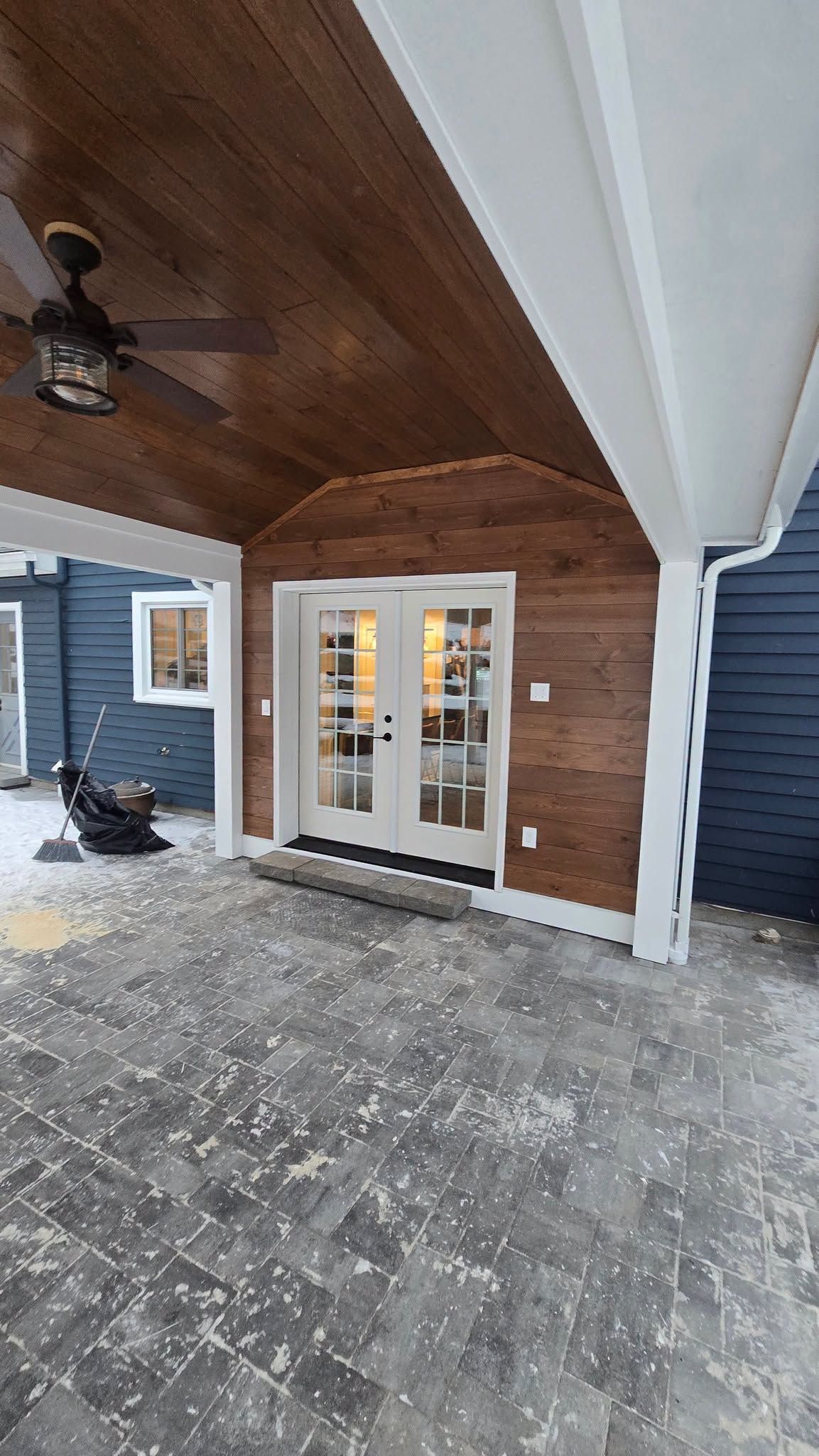 Covered porch with wood ceiling, white French doors, blue siding, and concrete patio.