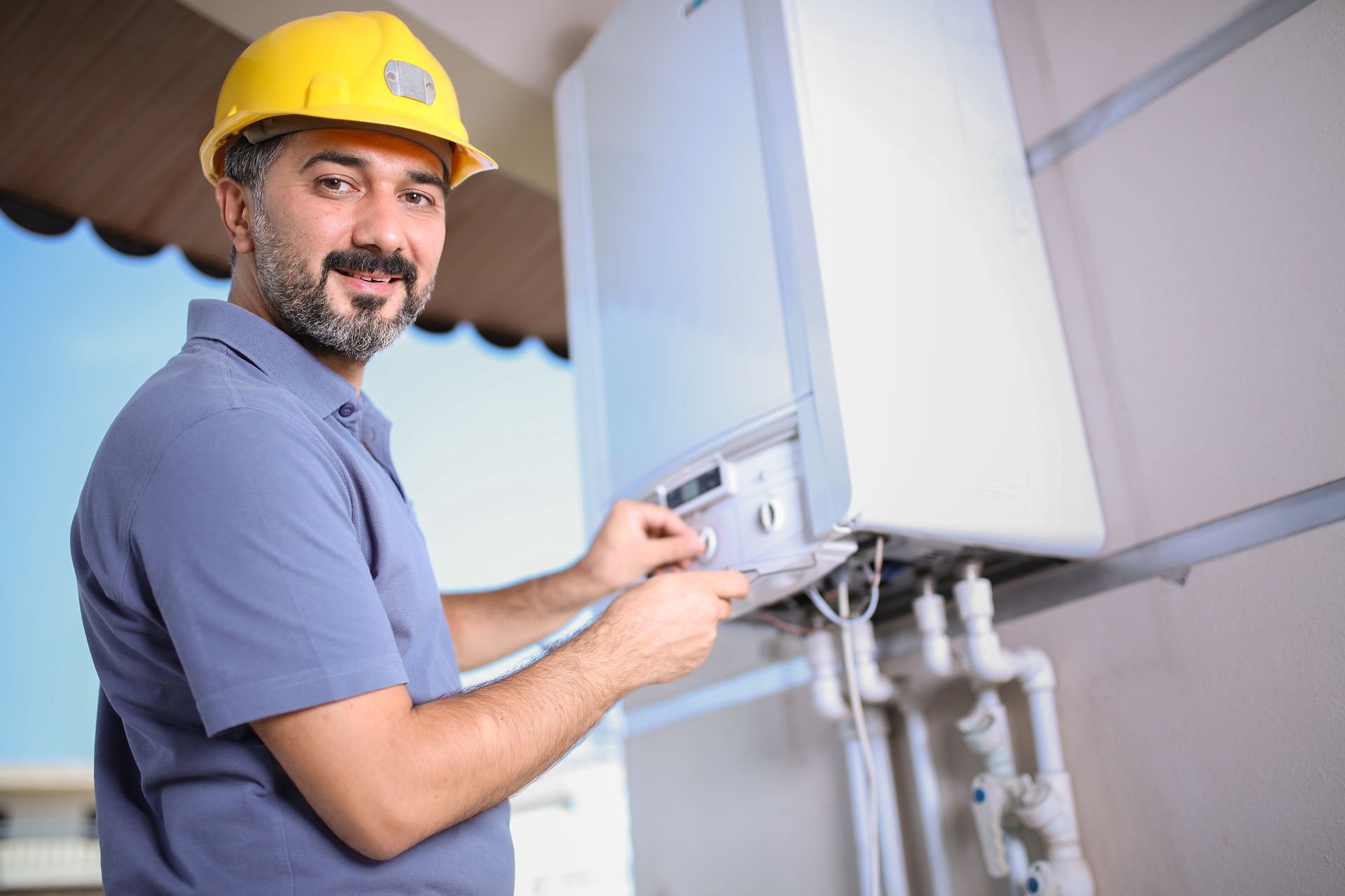 Worker adjusting controls on an outdoor boiler unit connected to exposed plumbing lines. Worker adjusting controls on an outdoor boiler unit connected to exposed plumbing lines.