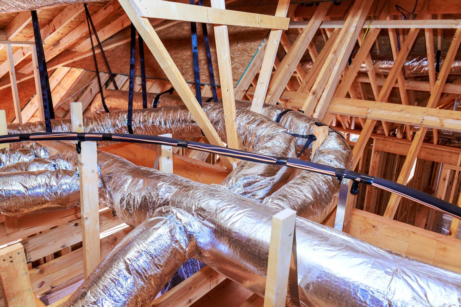 Attic with exposed wooden rafters and silver insulated HVAC ducts running through the space