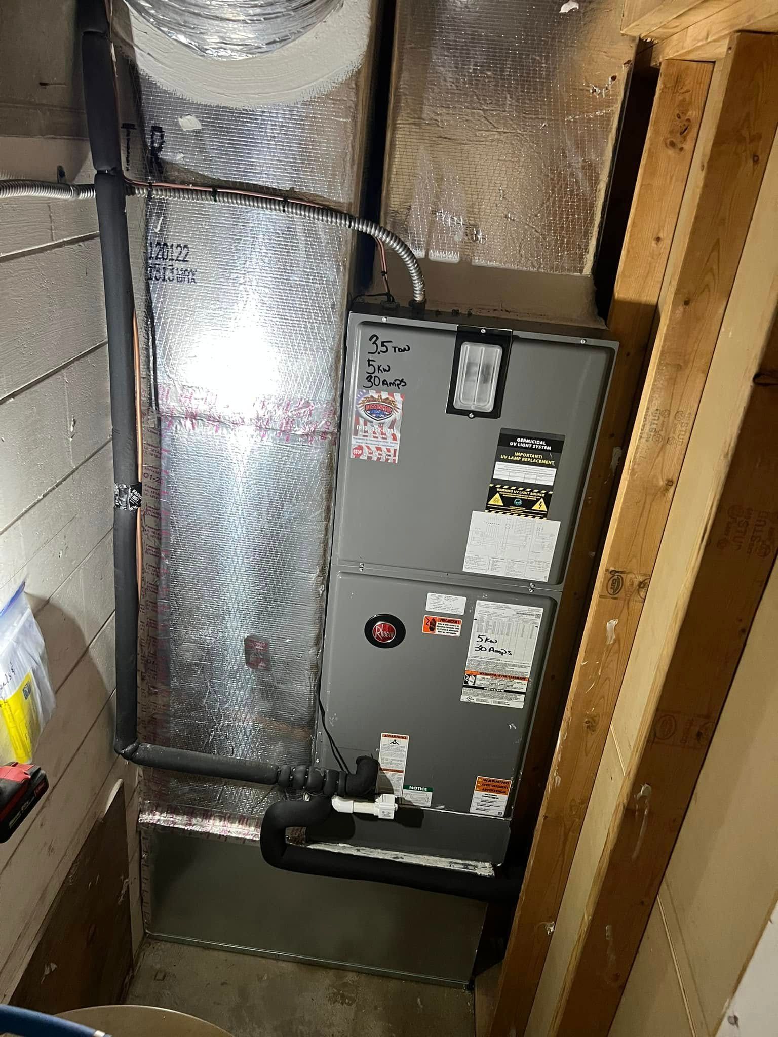 Air handler unit in a narrow utility closet with insulated ductwork and exposed framing.