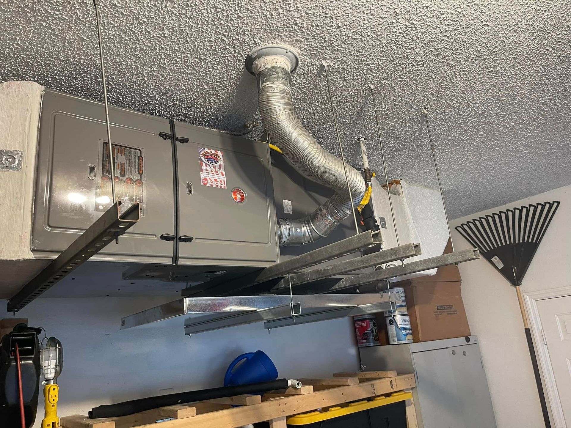 Garage ceiling with HVAC ductwork, a metal unit, and shelves holding stored items.