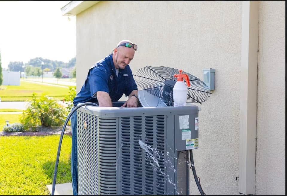 Technician cleaning an outdoor air conditioner unit beside a house