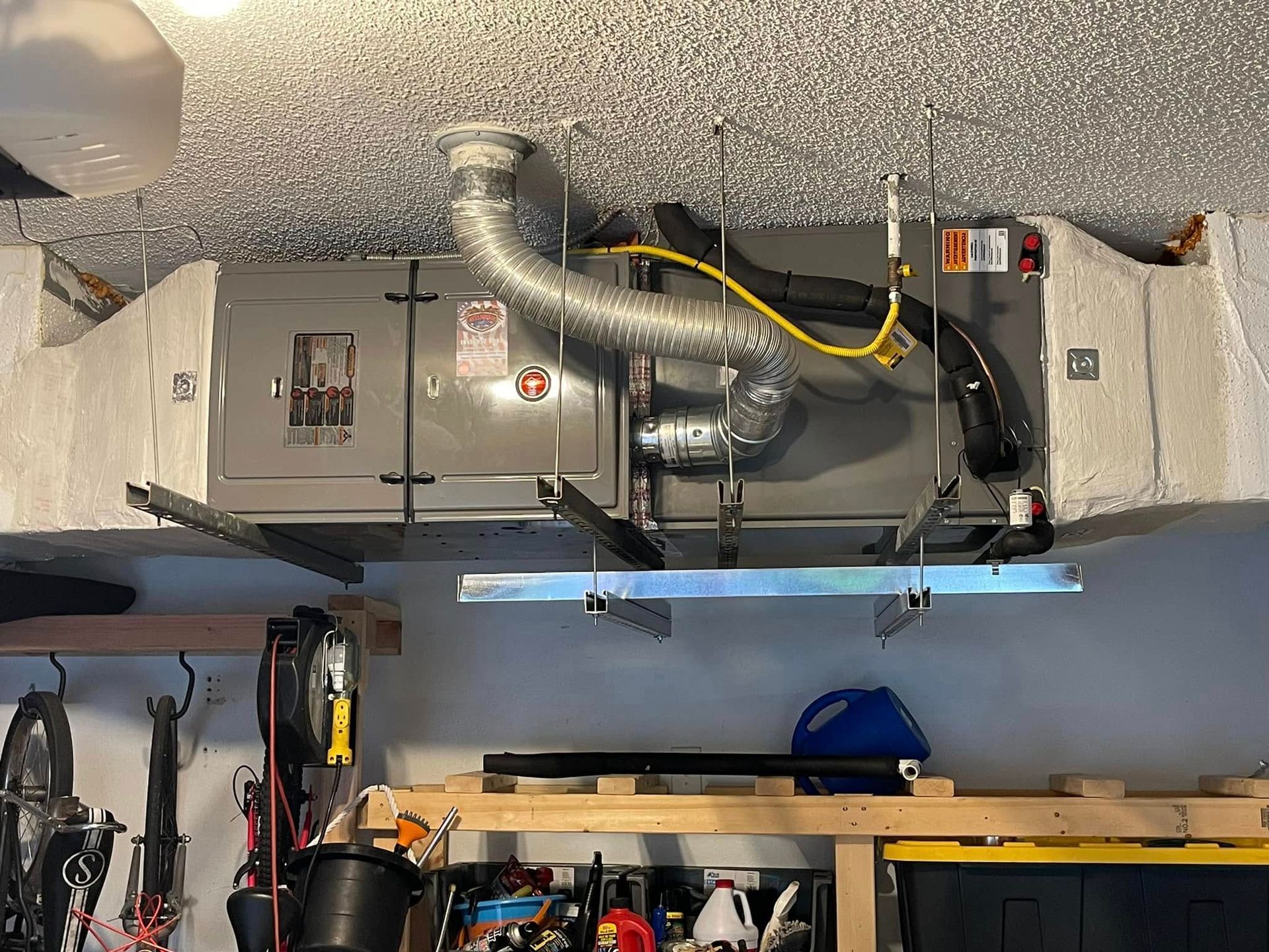 Overhead HVAC unit with exposed ductwork and wiring above a garage workspace